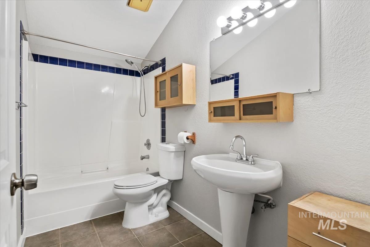 Full bathroom featuring bathing tub / shower combination, dark tile patterned floors, a textured wall, and lofted ceiling