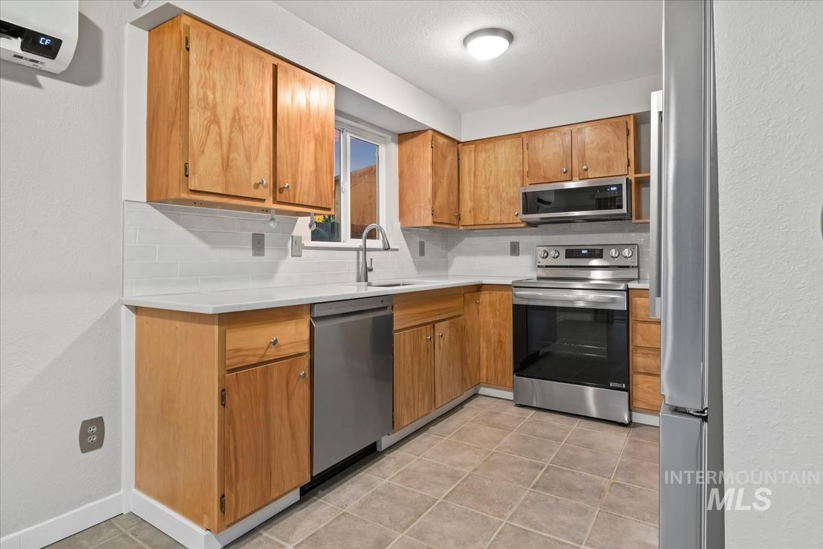 Kitchen with appliances with stainless steel finishes, a textured wall, decorative backsplash, brown cabinets, and a wall mounted air conditioner