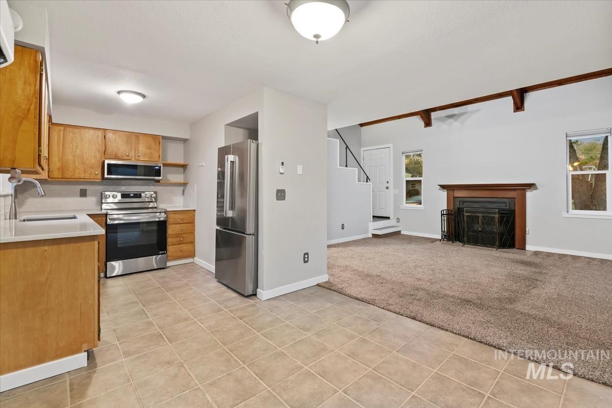 Kitchen with open shelves, light countertops, stainless steel appliances, a fireplace, and light colored carpet