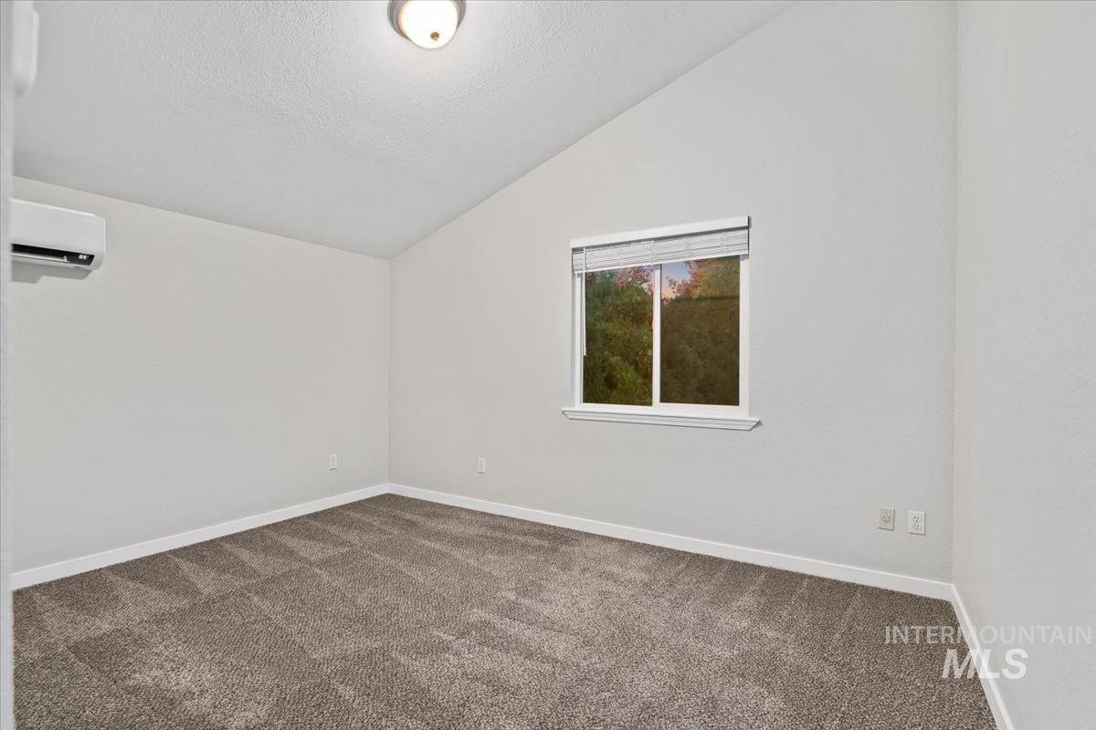 Carpeted spare room with vaulted ceiling, a textured ceiling, and a wall mounted AC