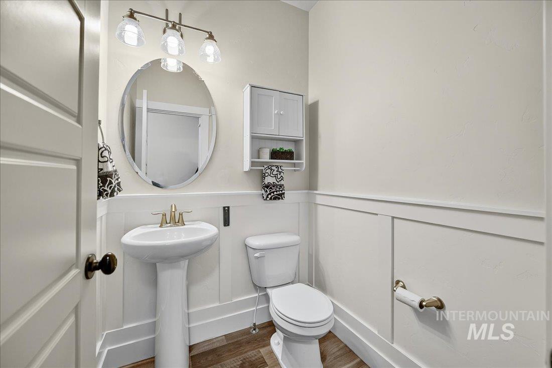 Half bathroom with a decorative wall, wainscoting, and wood finished floors