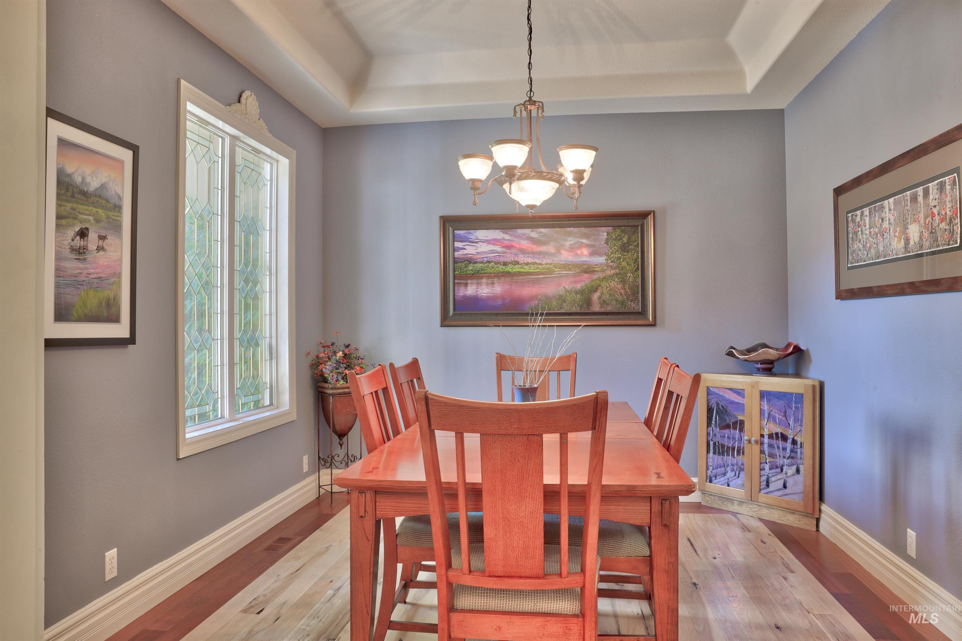 Dining area featuring tray ceilings, a decorative stained-glass window, wood-finish flooring, a chandelier light fixture, and baseboard and crown molding