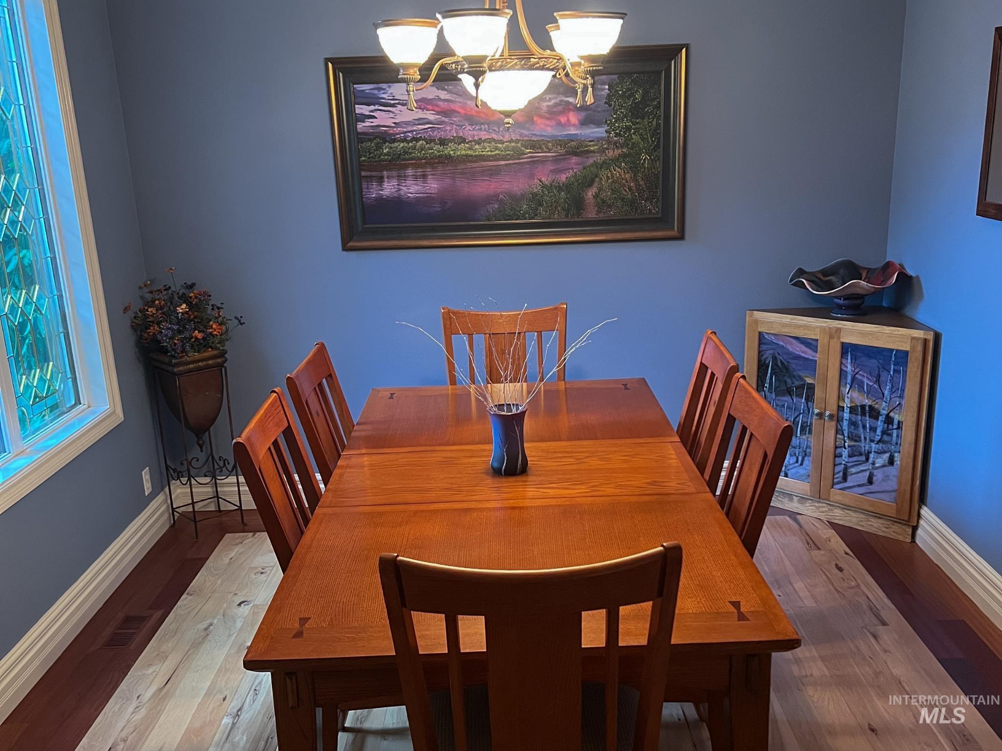 Dining area featuring a classic chandelier, prominent window with decorative glass, two-tone wood-finish flooring, and built-in wall art