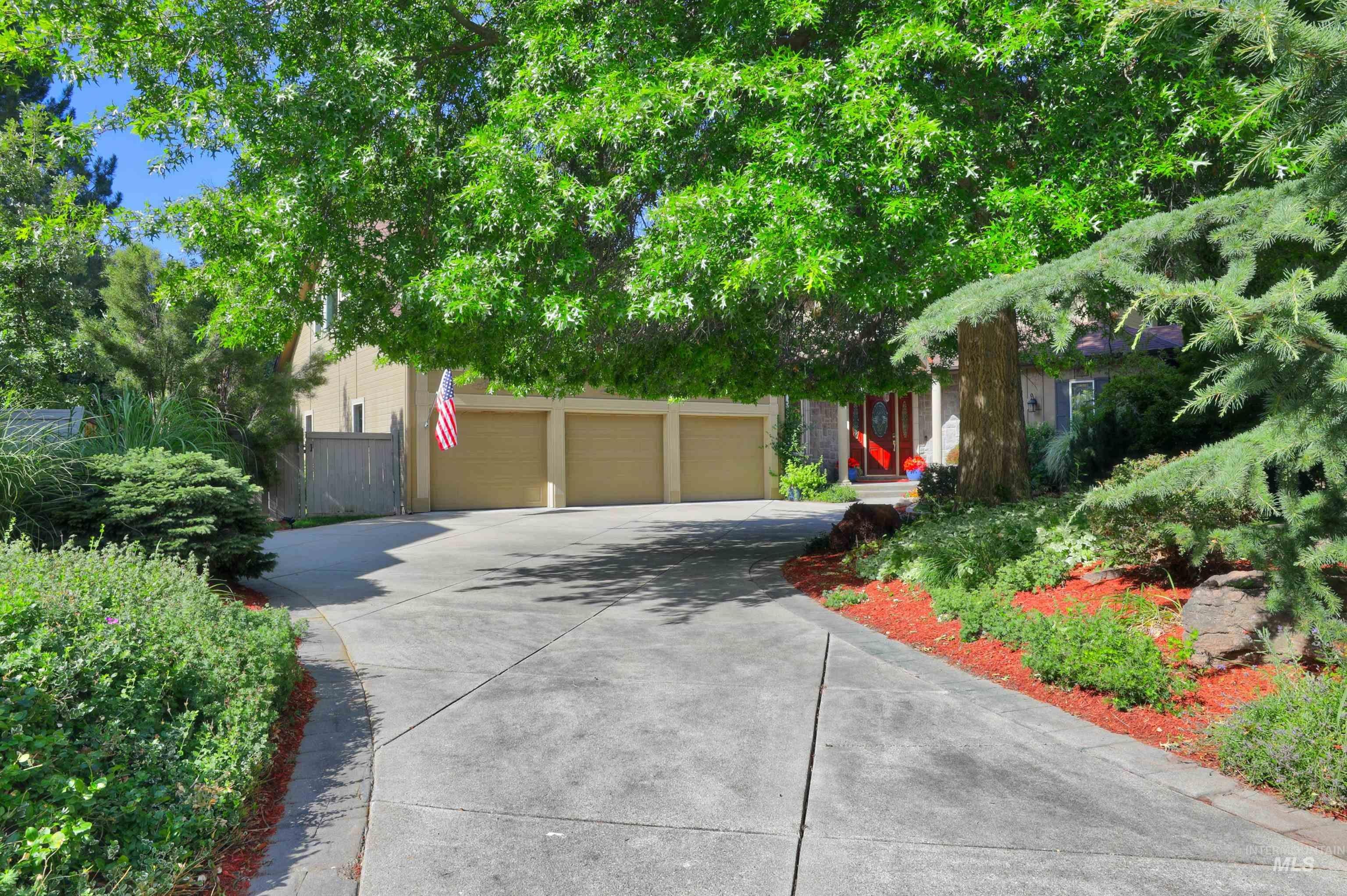 Spacious concrete driveway featuring a three-car garage, mature trees, and landscaped borders