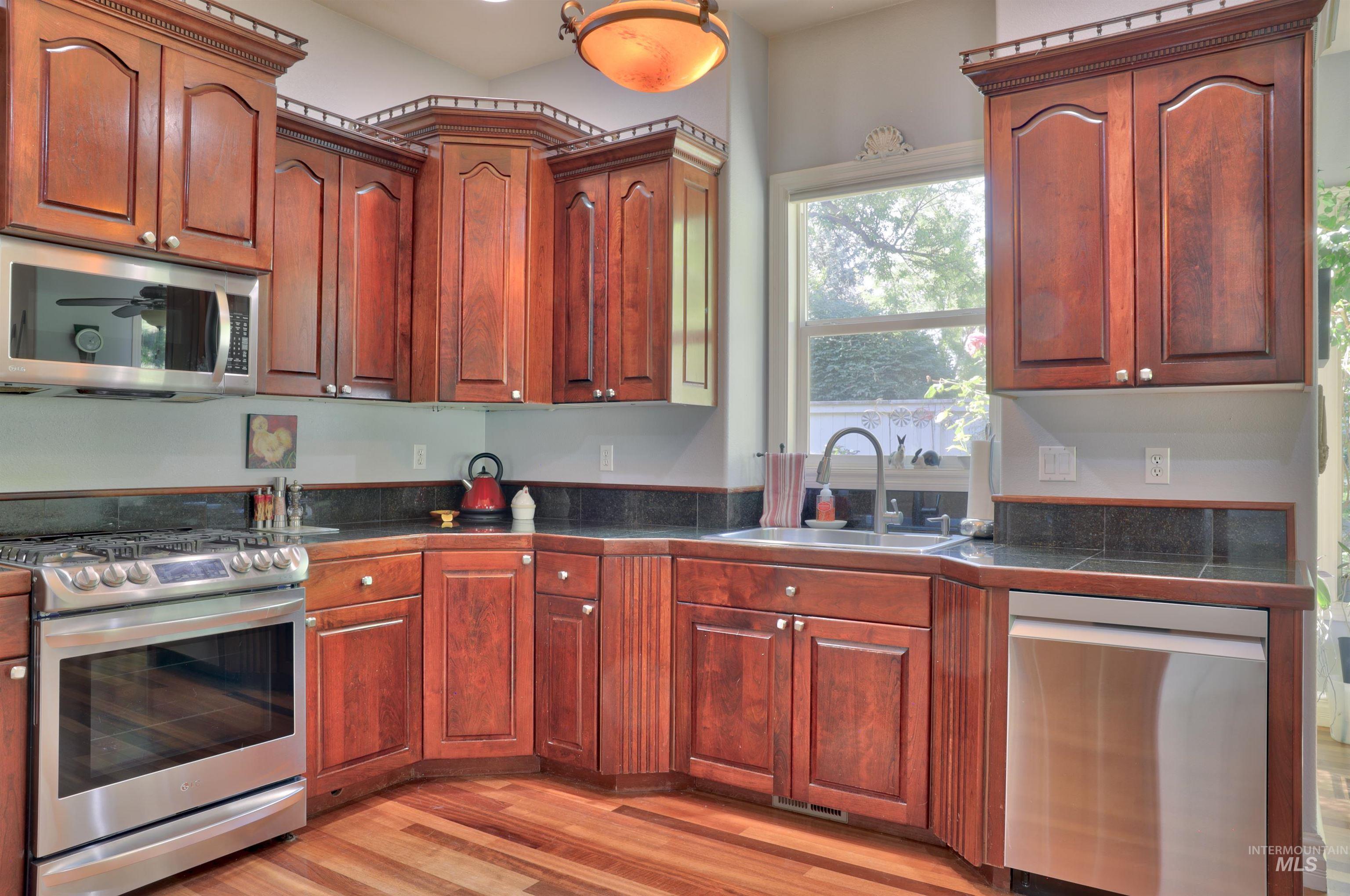 Kitchen featuring wood-finish cabinetry, stainless steel appliances, dark countertops, and wood-finish flooring