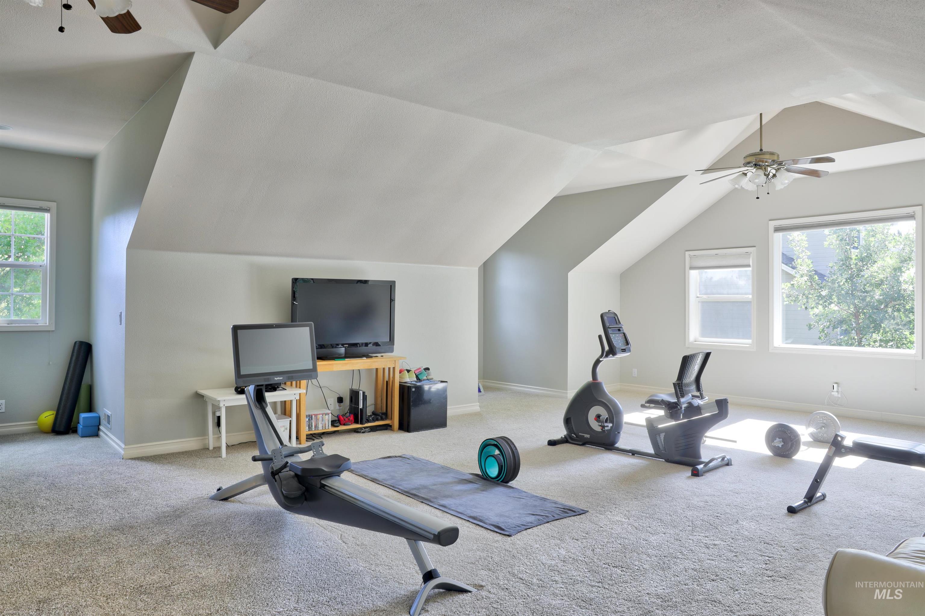 Spacious bonus room featuring vaulted ceilings, plush carpet flooring, recessed windows, and two ceiling fans