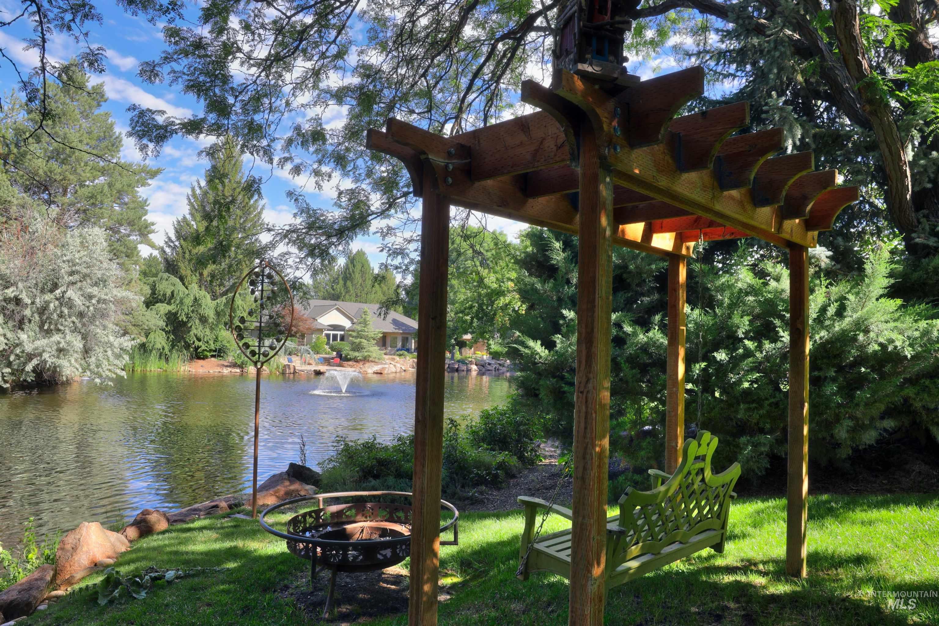 Lakeside outdoor area featuring a wooden pergola, swing bench, and a fire pit