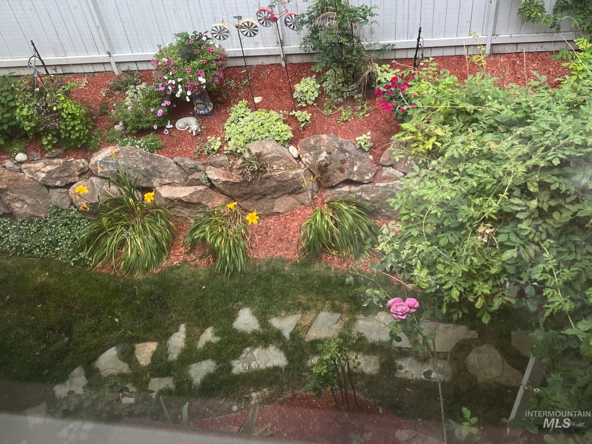 Tiered garden bed featuring a rock retaining wall, diverse plantings, and red mulch
