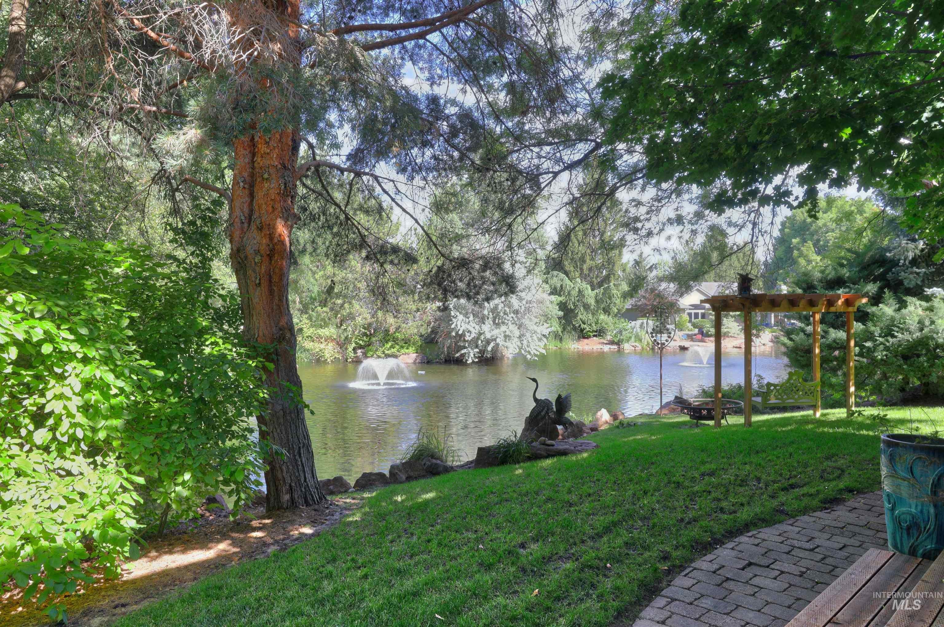 Expansive green lawn bordering a tranquil body of water, featuring a decorative fountain