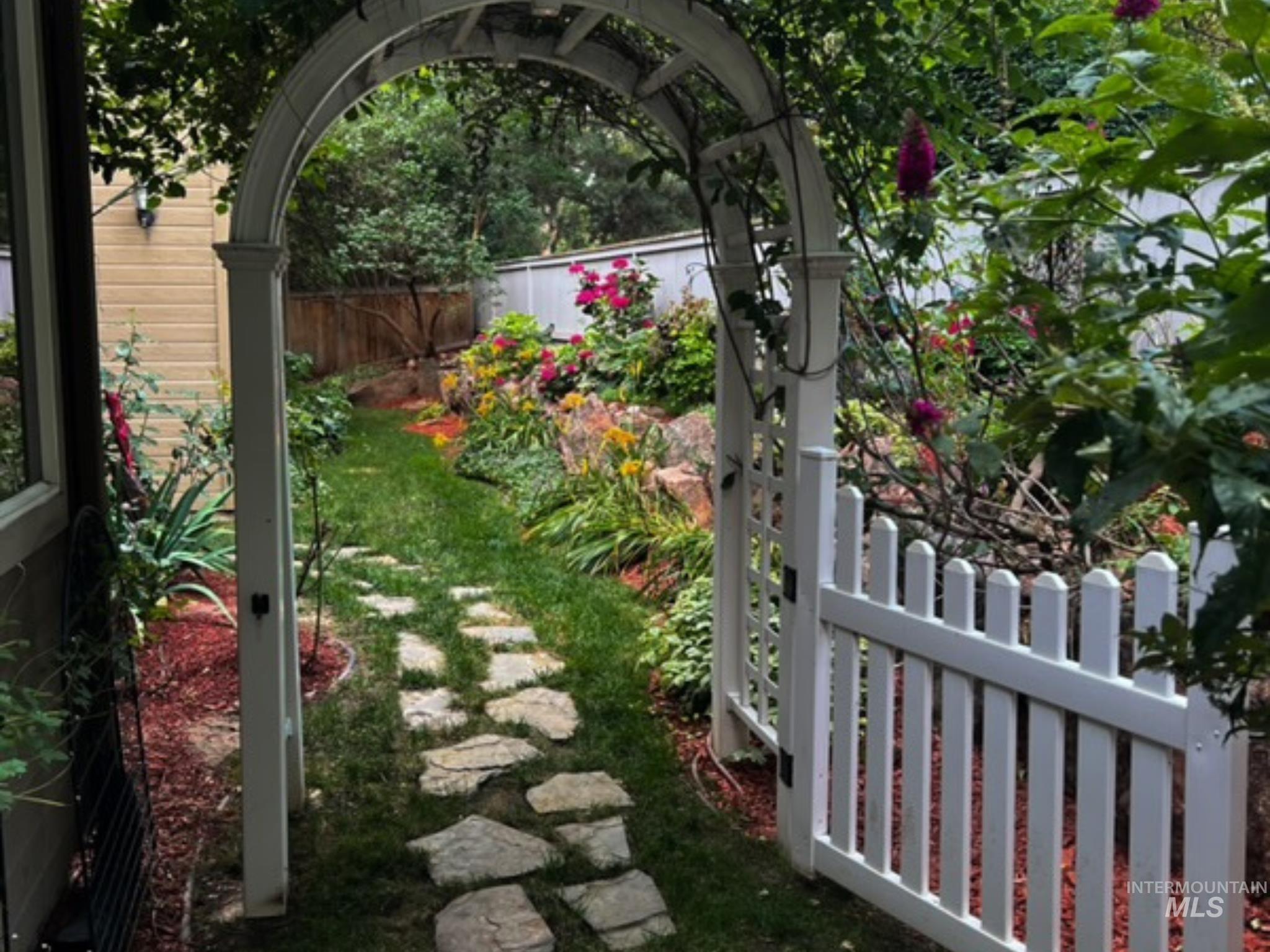 Garden pathway featuring a white arched trellis and picket gate