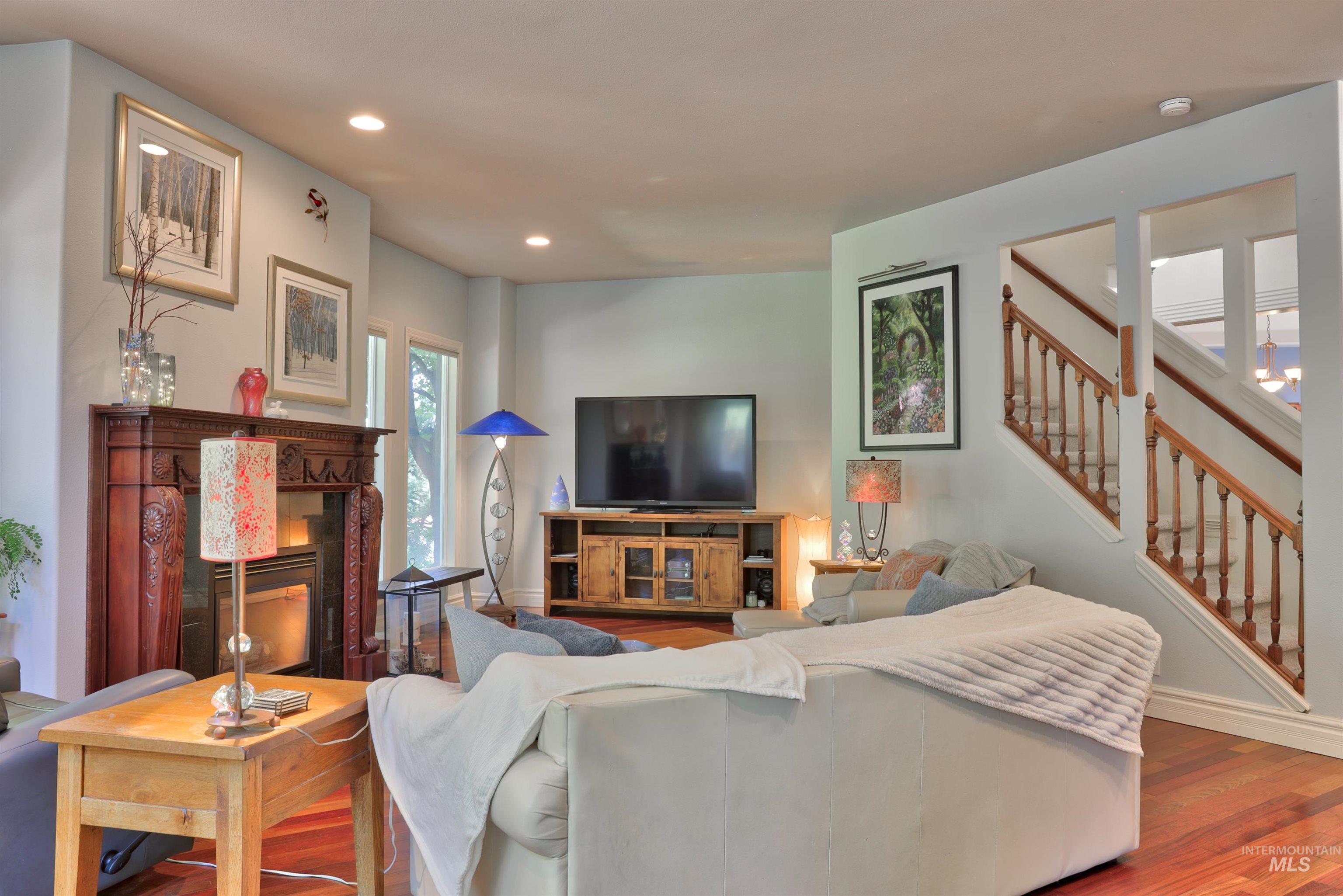 Living area featuring wood-finish flooring, a detailed wood fireplace surround, recessed ceiling lighting, and a staircase with wood handrails