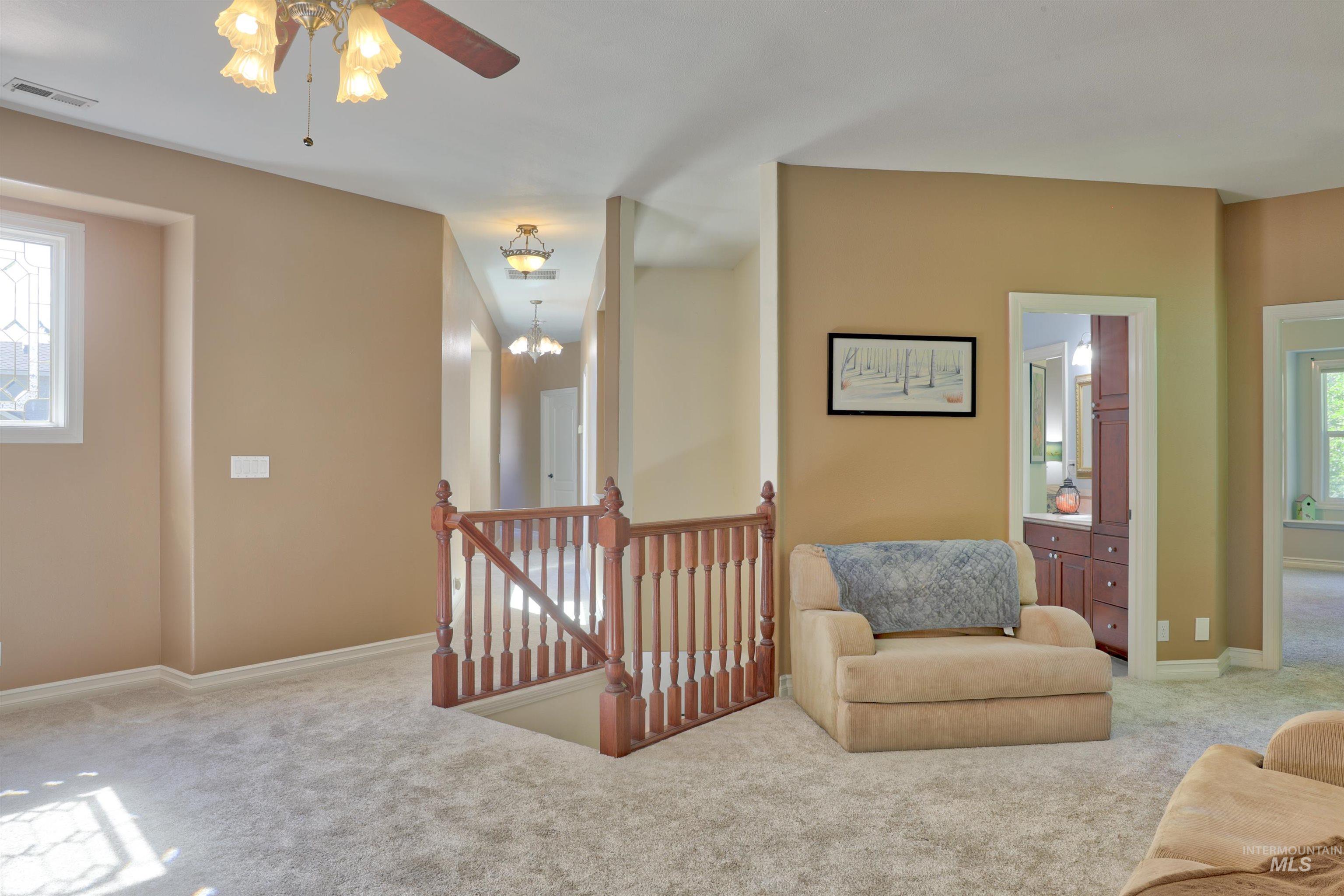 Carpeted upper-level landing featuring a wood banister, decorative ceiling fan, and multiple lighting fixtures