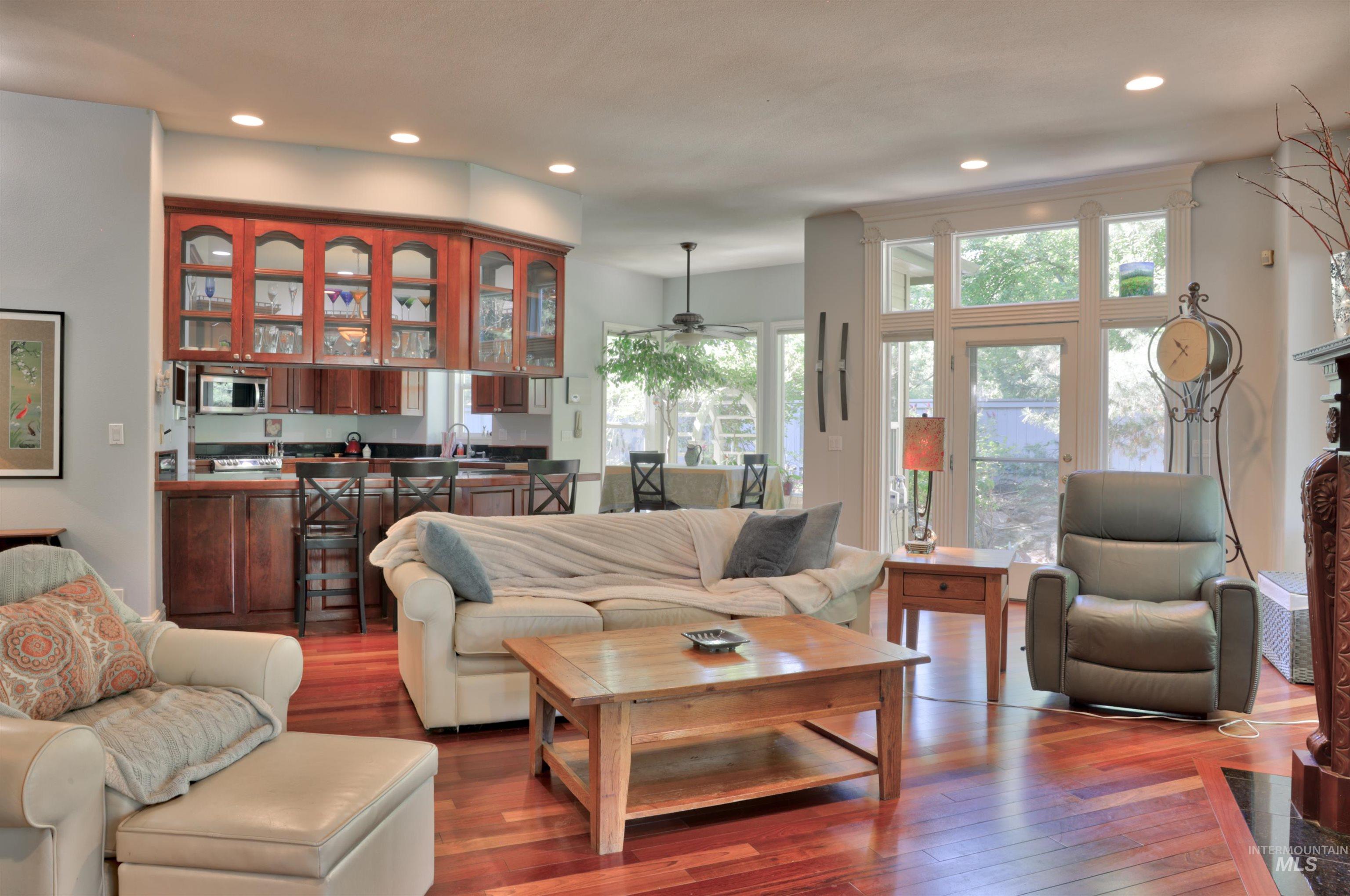 Open-concept living area featuring rich wood-finish flooring, a built-in kitchen bar with dark cabinetry and glass-front upper cabinets, and a prominent fireplace with carved wood detailing