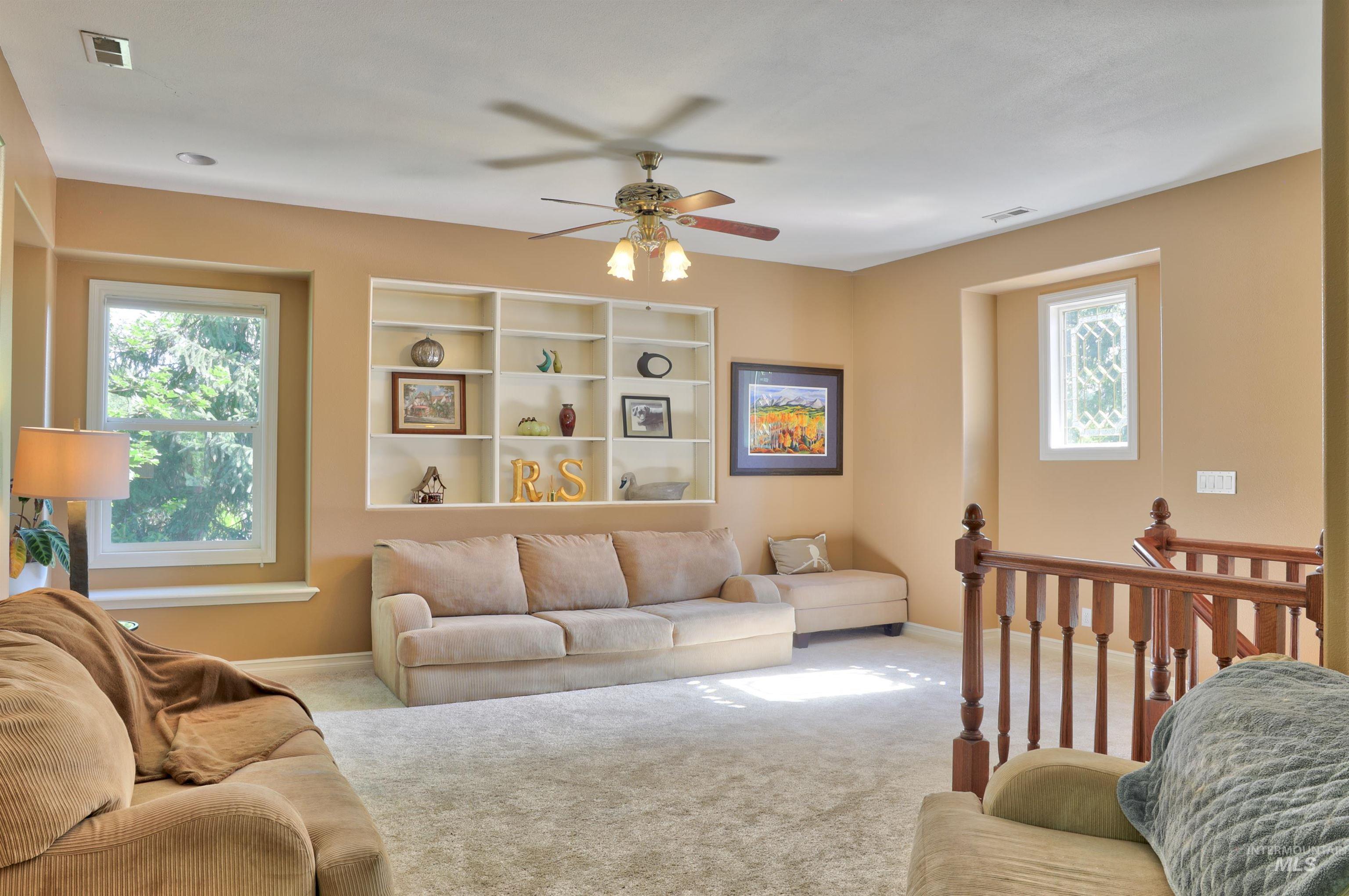 Spacious living area featuring neutral carpeting, a large built-in shelving unit, and multiple windows providing natural light