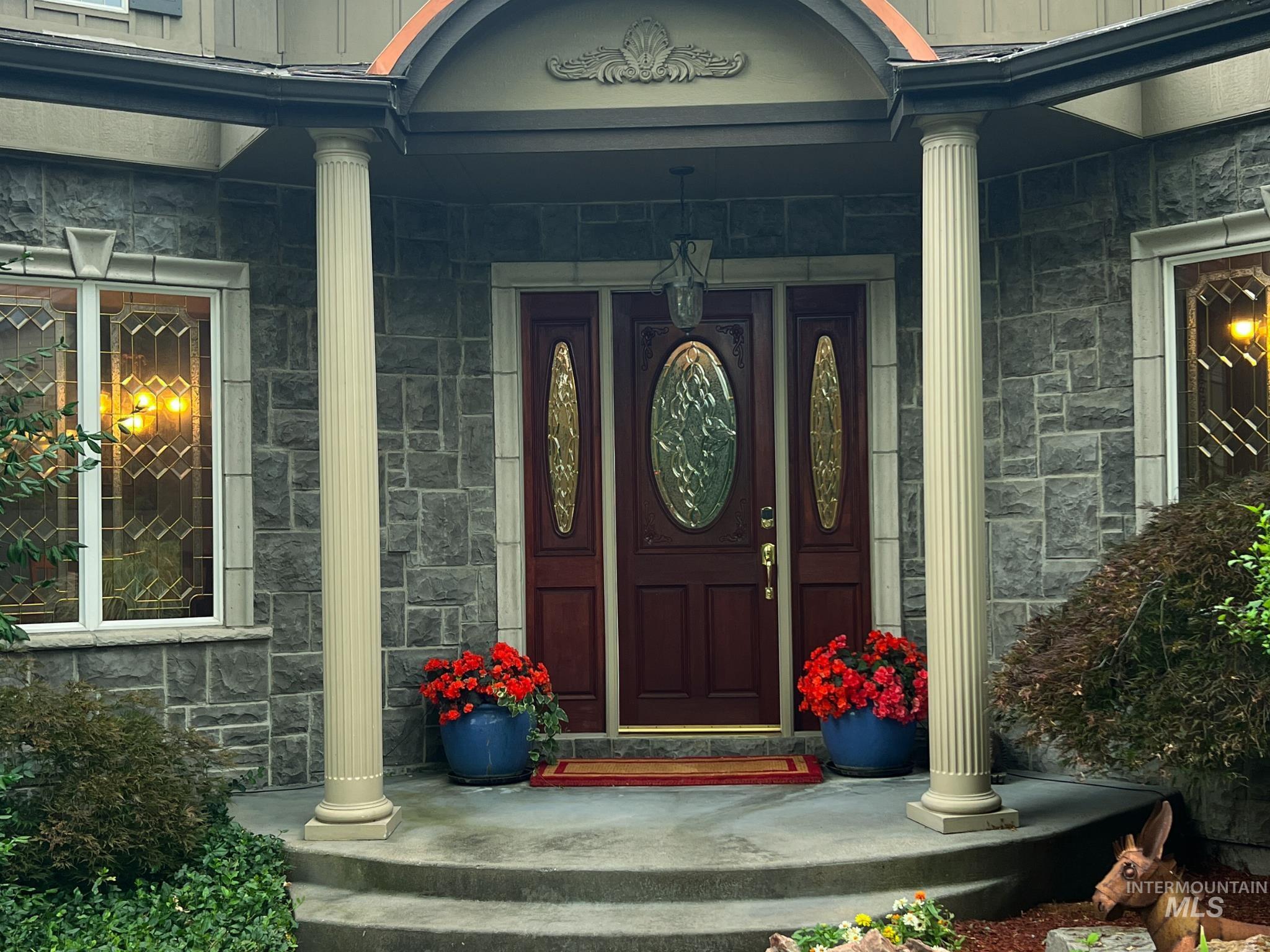 Stone facade entrance featuring a mahogany-finish door with decorative glass, flanked by fluted columns