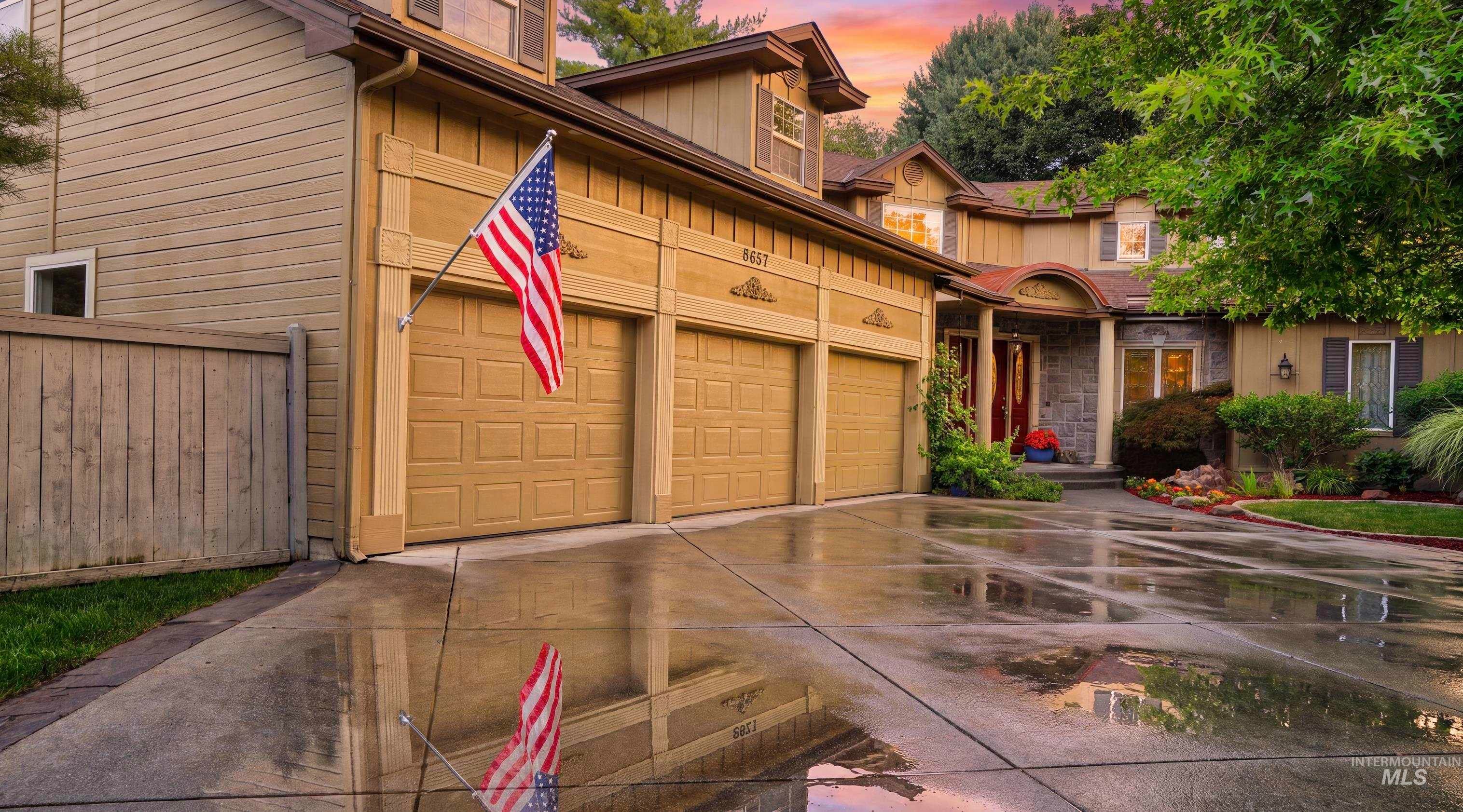Three-car garage with panel doors, concrete driveway, and established landscaping