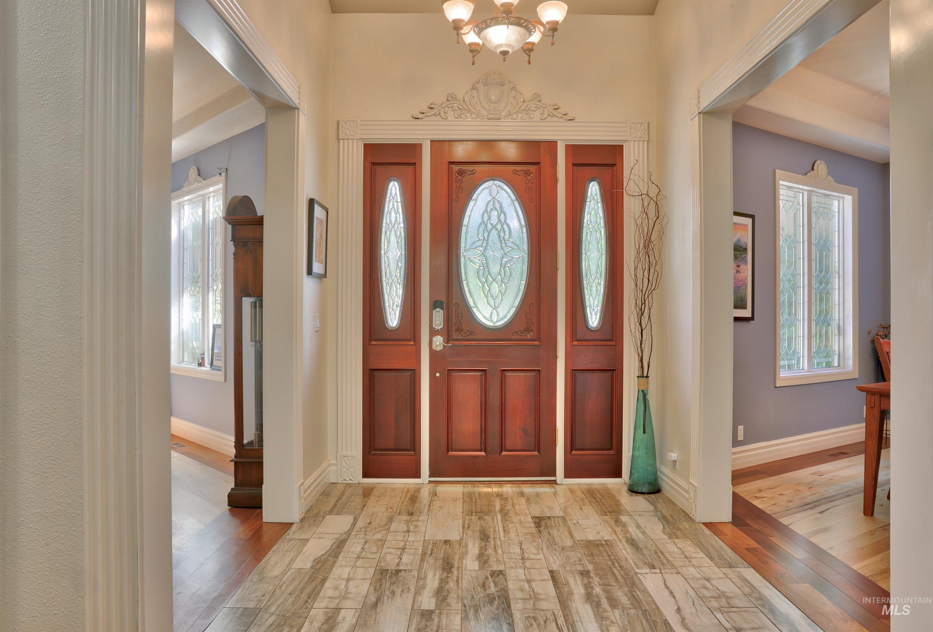 Wood-finish entryway flooring leading to an ornate wood-paneled front door with decorative glass inserts and side panels