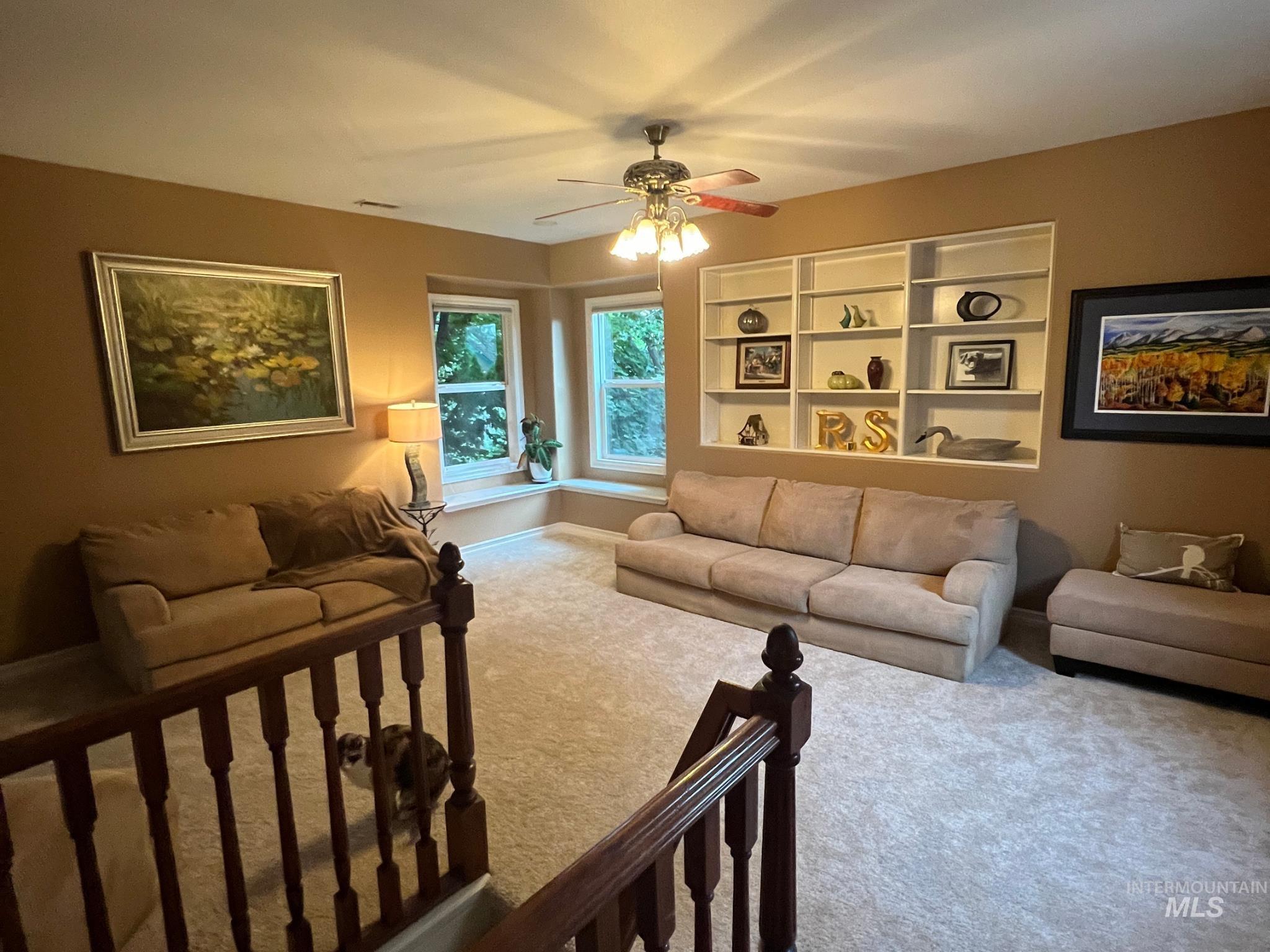 Carpeted room featuring built-in shelving, bay windows with deep sills, and a ceiling fan with integrated lighting