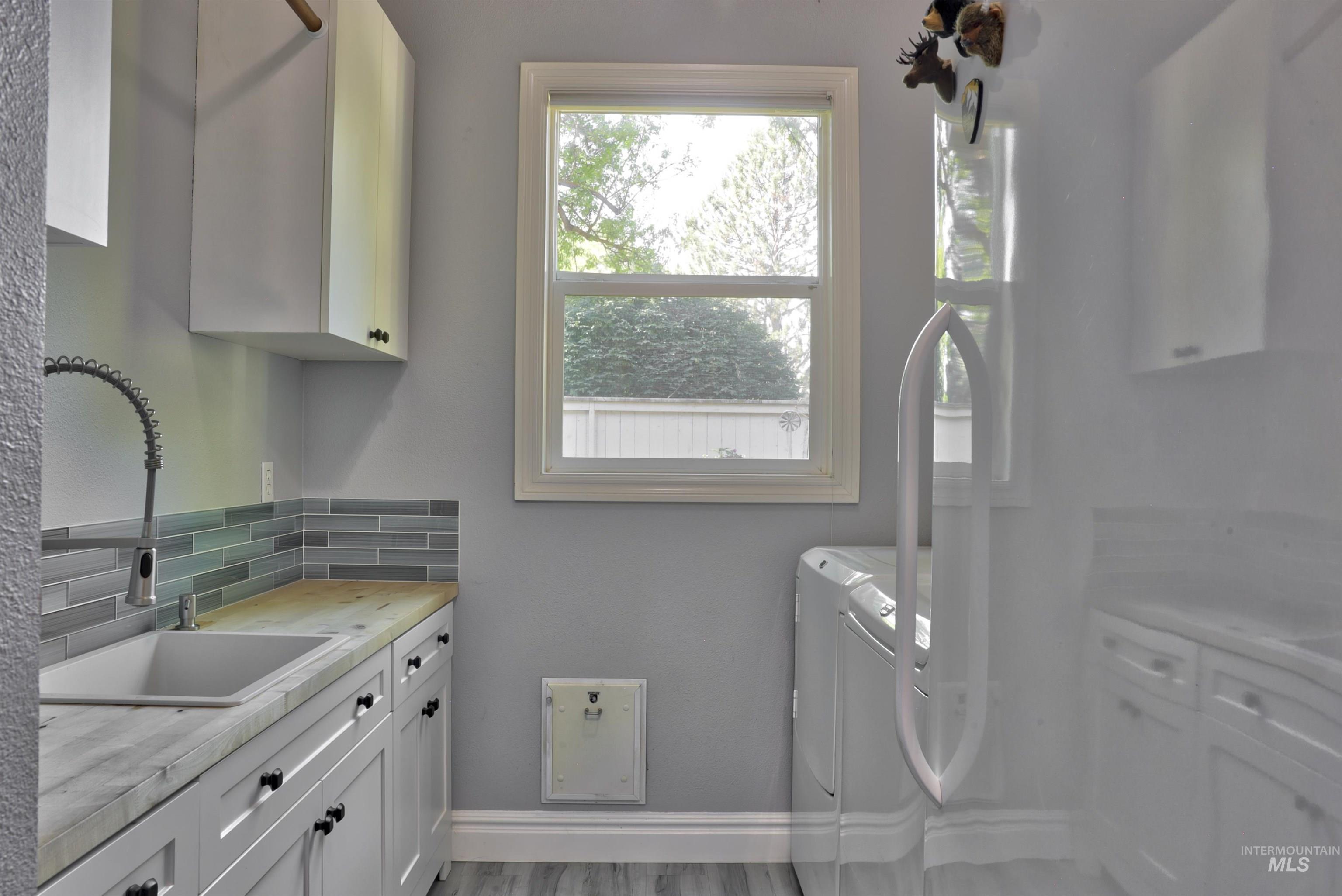 Laundry area featuring white cabinetry, a utility sink with a gooseneck faucet, light wood-finish countertops, and a subway tile backsplash