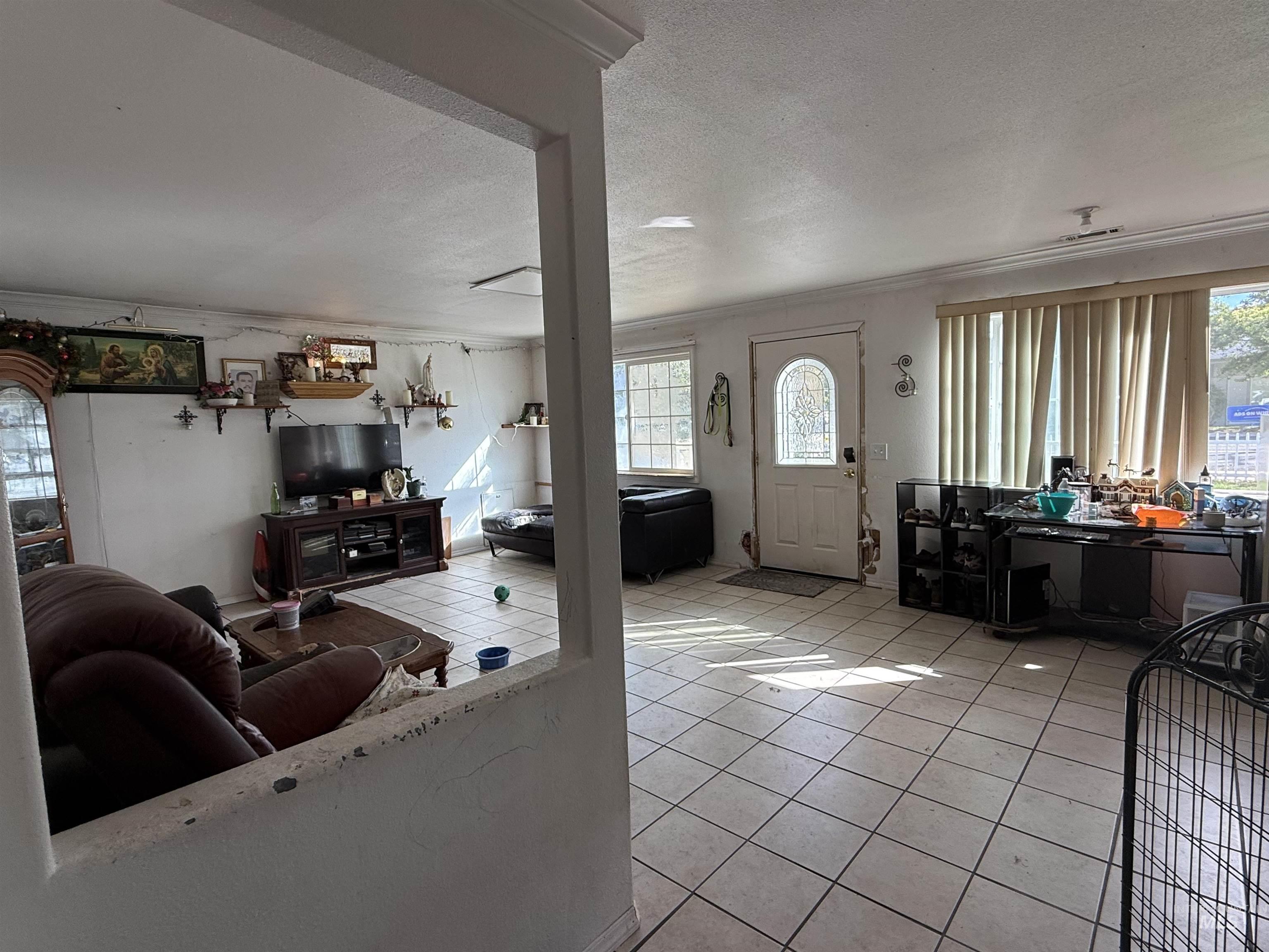 Living area featuring a textured ceiling, light tile patterned floors, plenty of natural light, and crown molding