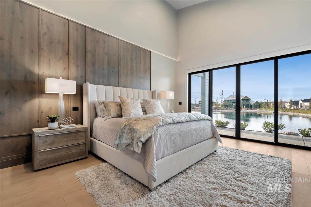 Bedroom featuring a high ceiling, light wood finished floors, access to outside, a water view, and wood walls