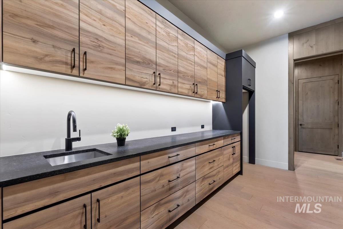 Bar featuring dark stone counters, light wood finished floors, and modern cabinets