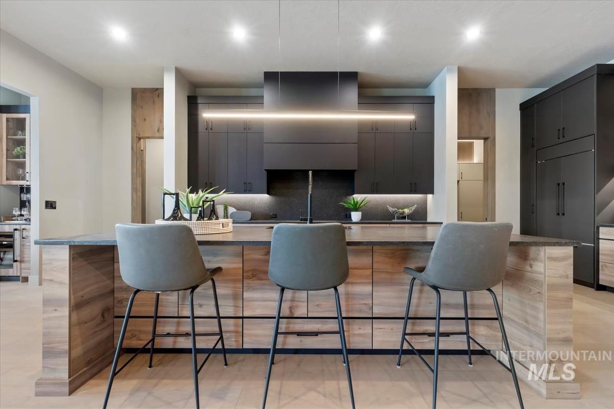 Kitchen featuring a breakfast bar, a large island, backsplash, extractor fan, and dark stone counters