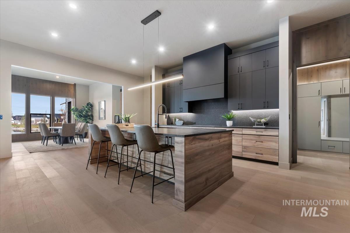 Kitchen with modern cabinets, an island with sink, hanging light fixtures, a kitchen breakfast bar, and gray cabinetry