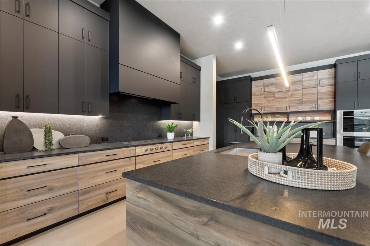 Kitchen featuring double oven, dark stone countertops, tasteful backsplash, recessed lighting, and range hood