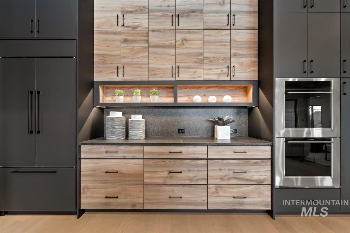Kitchen featuring light brown cabinetry, paneled built in fridge, stainless steel double oven, and decorative backsplash