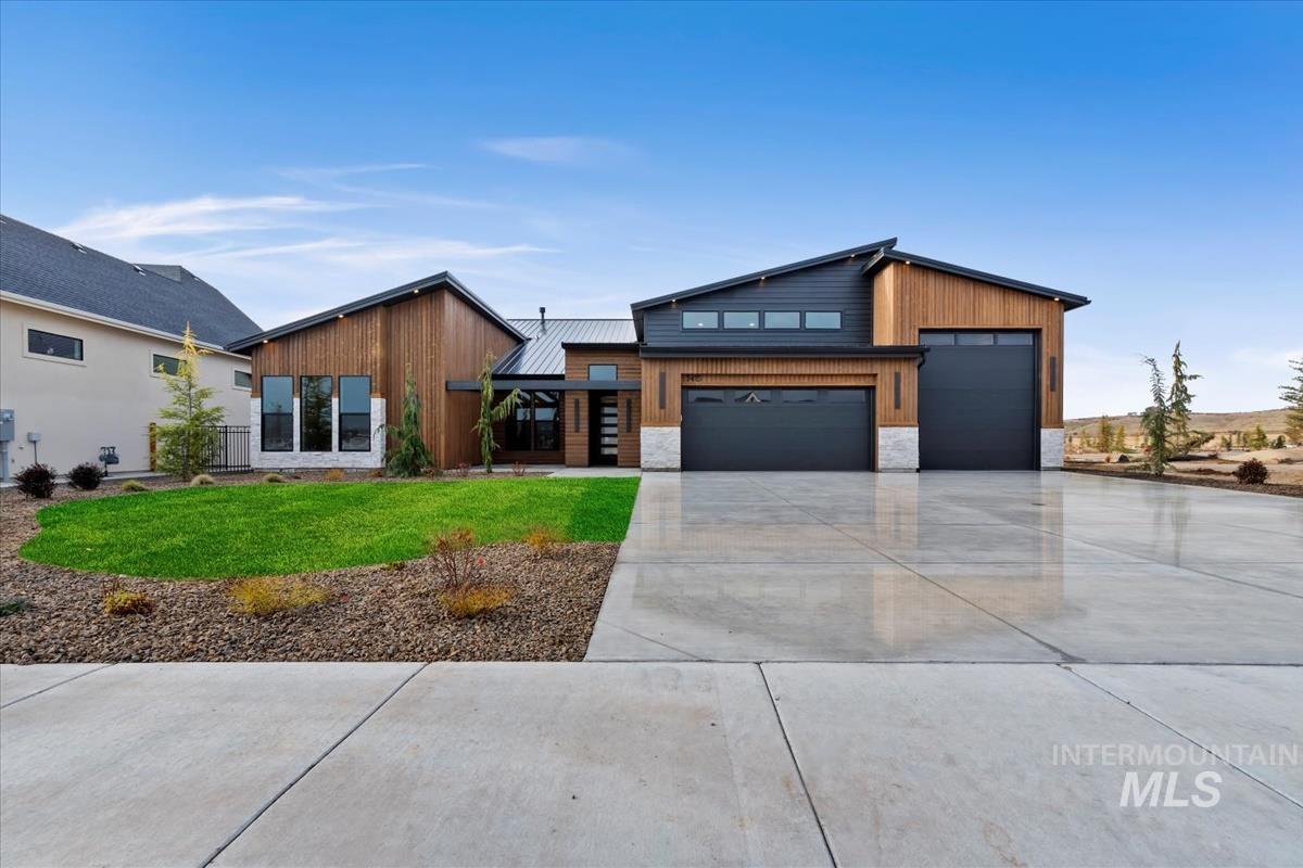 Contemporary home with a front yard, stone siding, driveway, a garage, and a metal roof