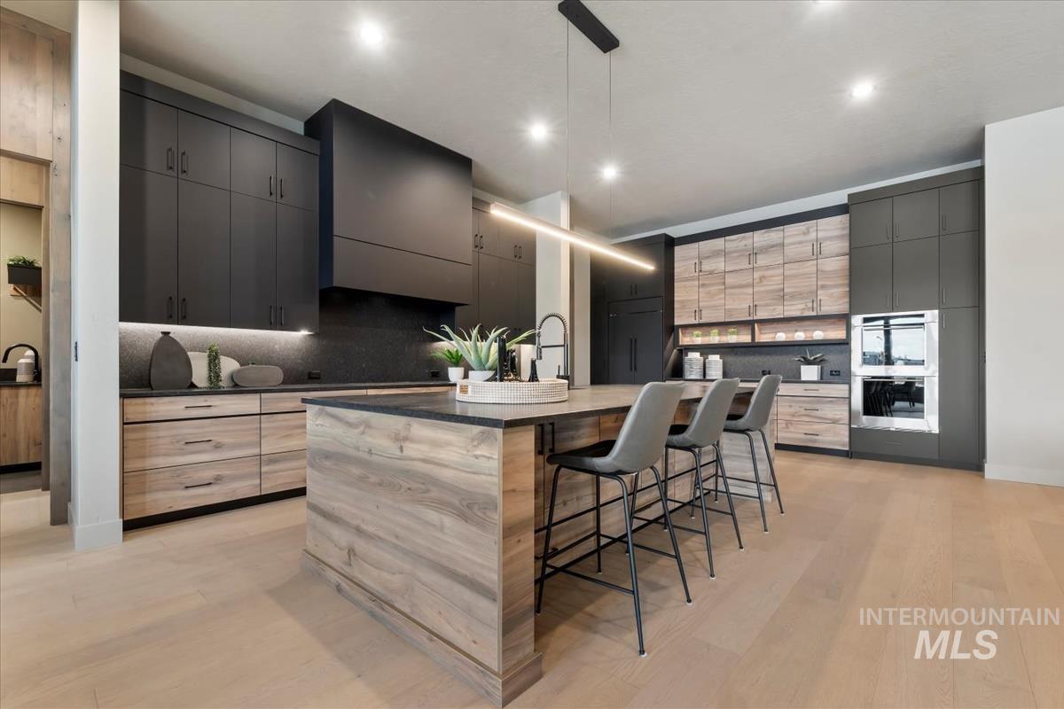 Kitchen featuring a breakfast bar area, a kitchen island with sink, hanging light fixtures, modern cabinets, and gray cabinetry