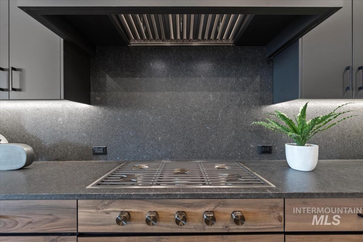 Kitchen view of range hood, stainless steel gas cooktop, tasteful backsplash, and dark stone counters