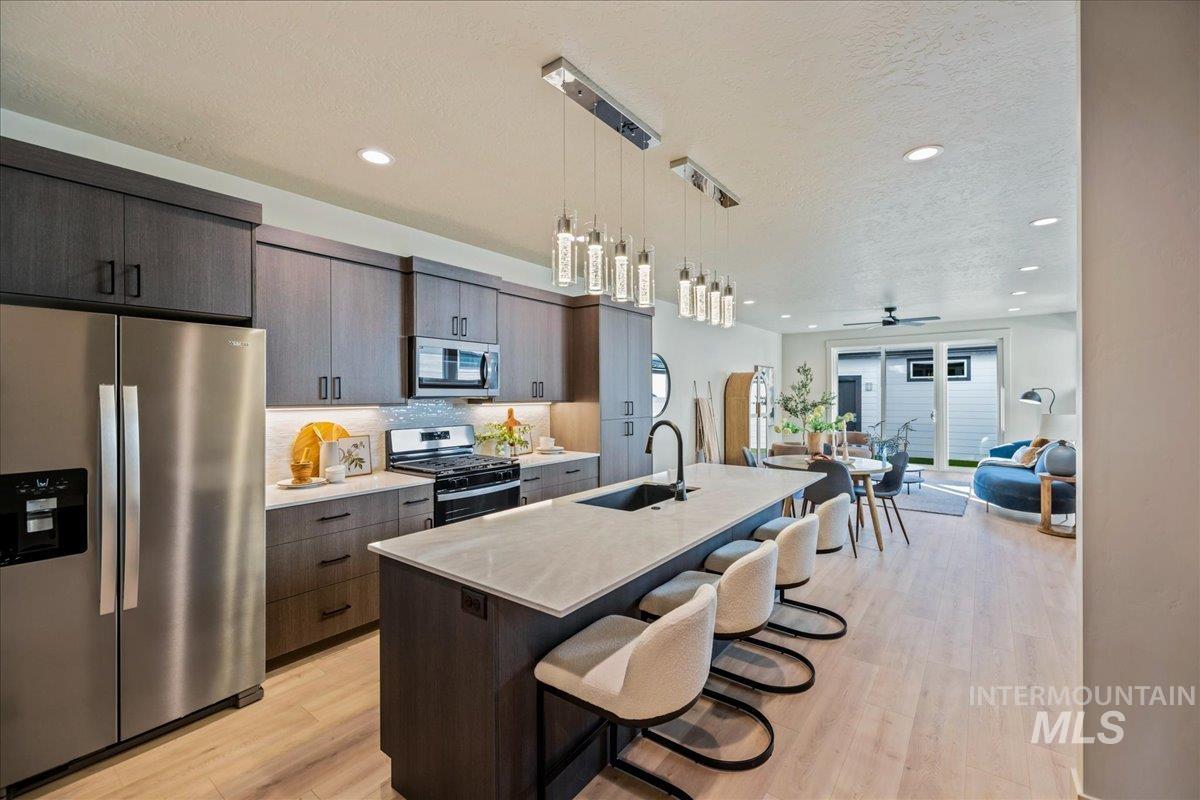 Kitchen with stainless steel appliances, a kitchen breakfast bar, pendant lighting, a textured ceiling, and an island with sink