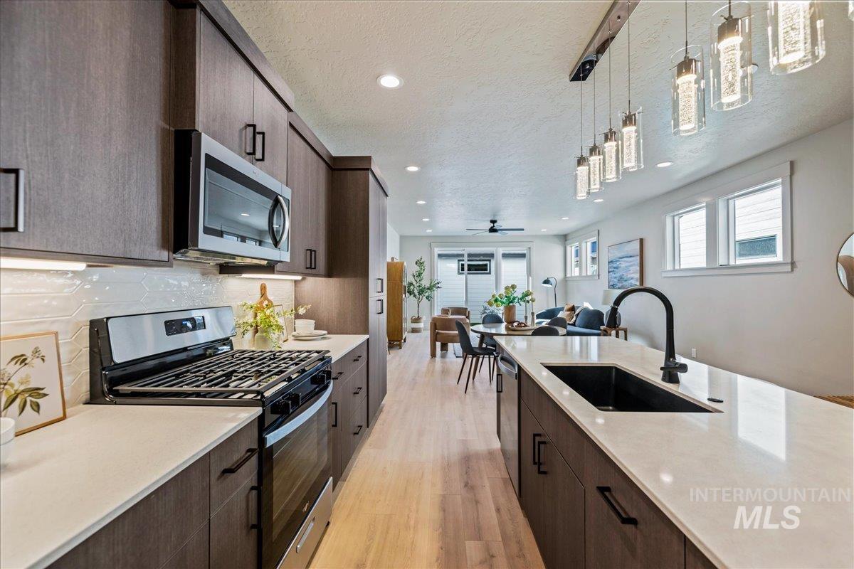 Kitchen with stainless steel appliances, dark brown cabinets, open floor plan, a textured ceiling, and hanging light fixtures