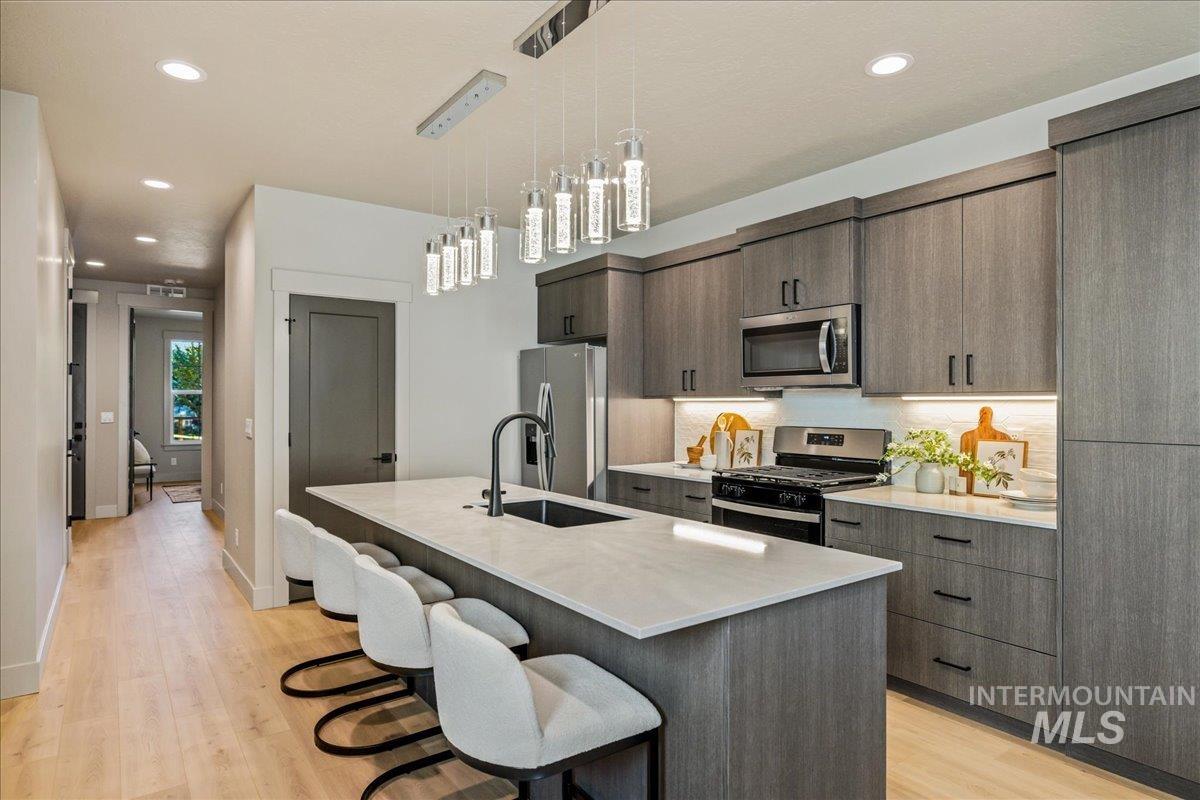 Kitchen with recessed lighting, appliances with stainless steel finishes, a kitchen breakfast bar, a kitchen island with sink, and decorative light fixtures