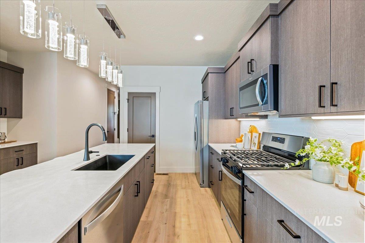 Kitchen with modern cabinets, appliances with stainless steel finishes, pendant lighting, light stone countertops, and light wood-style floors