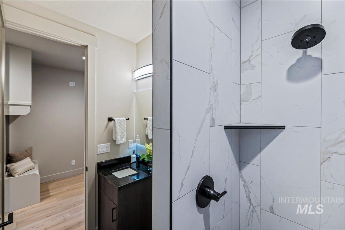 Full bath featuring vanity, tiled shower, and light wood-style flooring