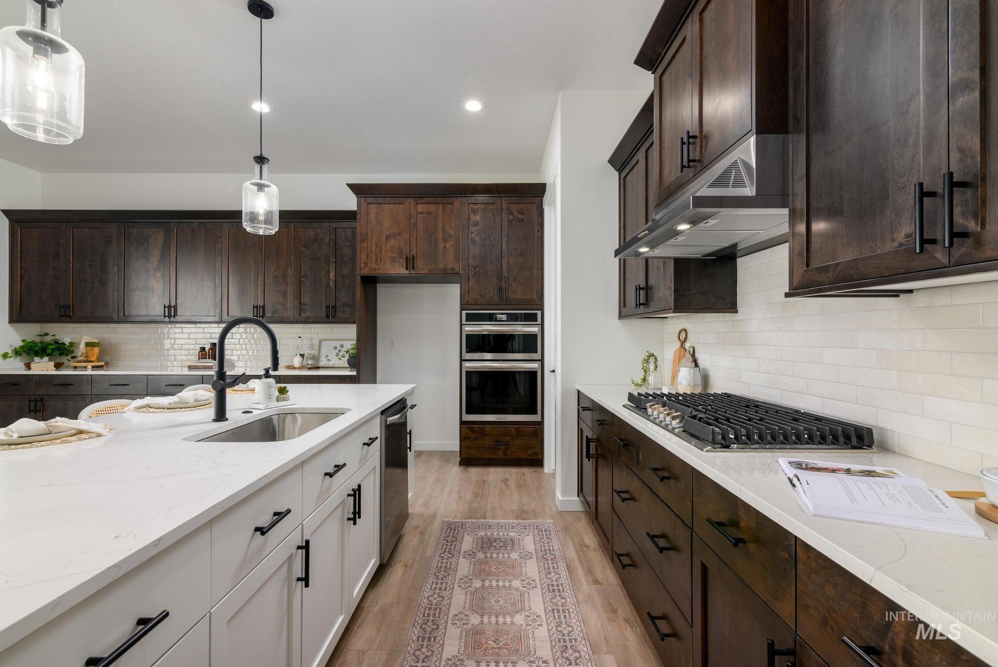 Kitchen featuring appliances with stainless steel finishes, under cabinet range hood, light stone counters, light wood finished floors, and dark brown cabinetry