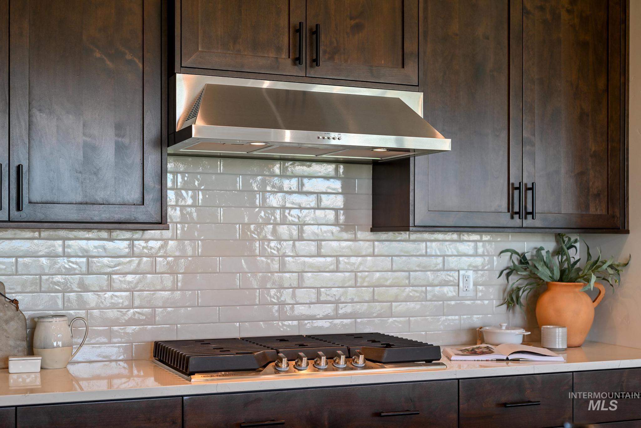 Kitchen with exhaust hood, dark brown cabinets, light countertops, tasteful backsplash, and stainless steel gas stovetop