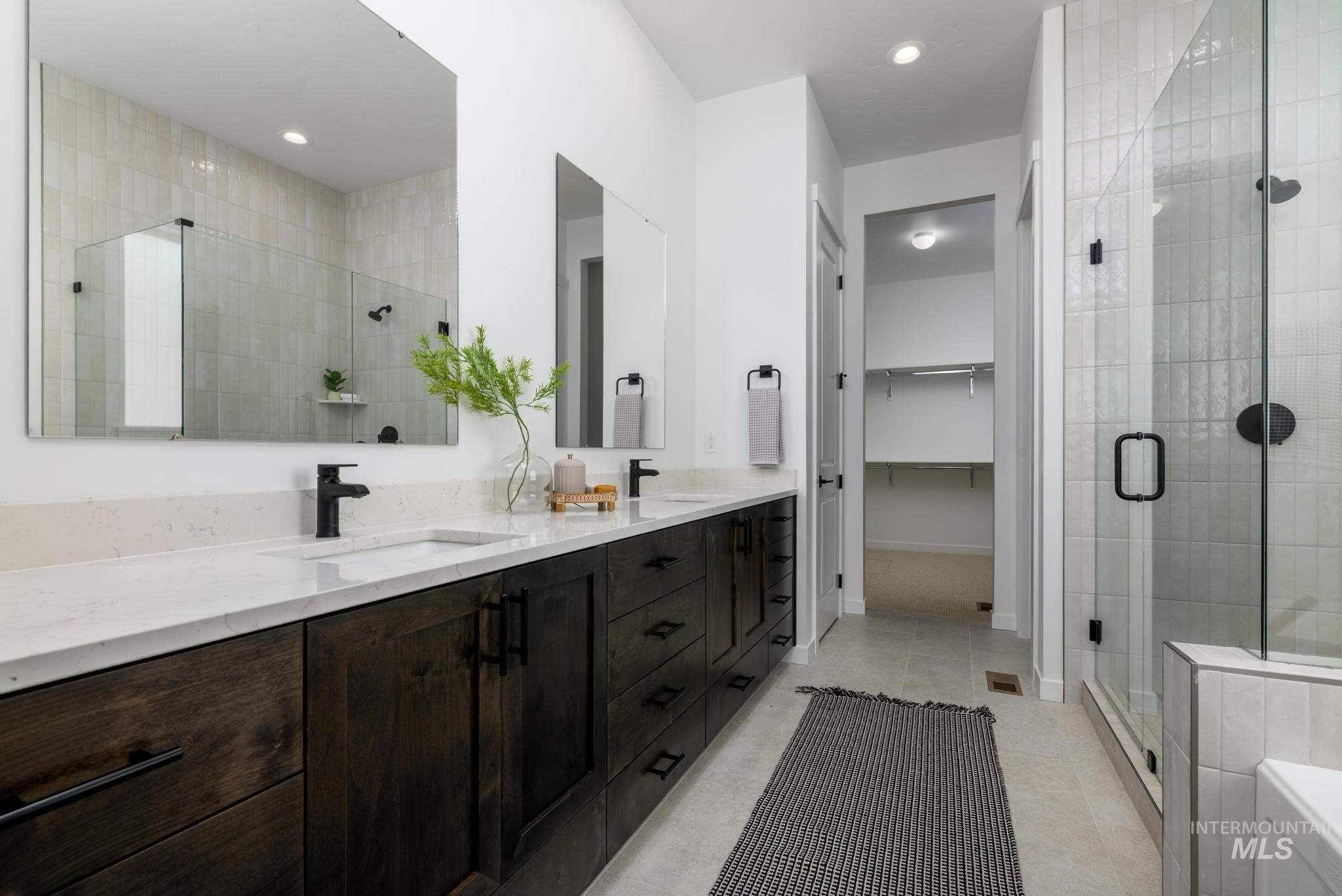 Bathroom featuring a stall shower, double vanity, tile patterned floors, a walk in closet, and recessed lighting