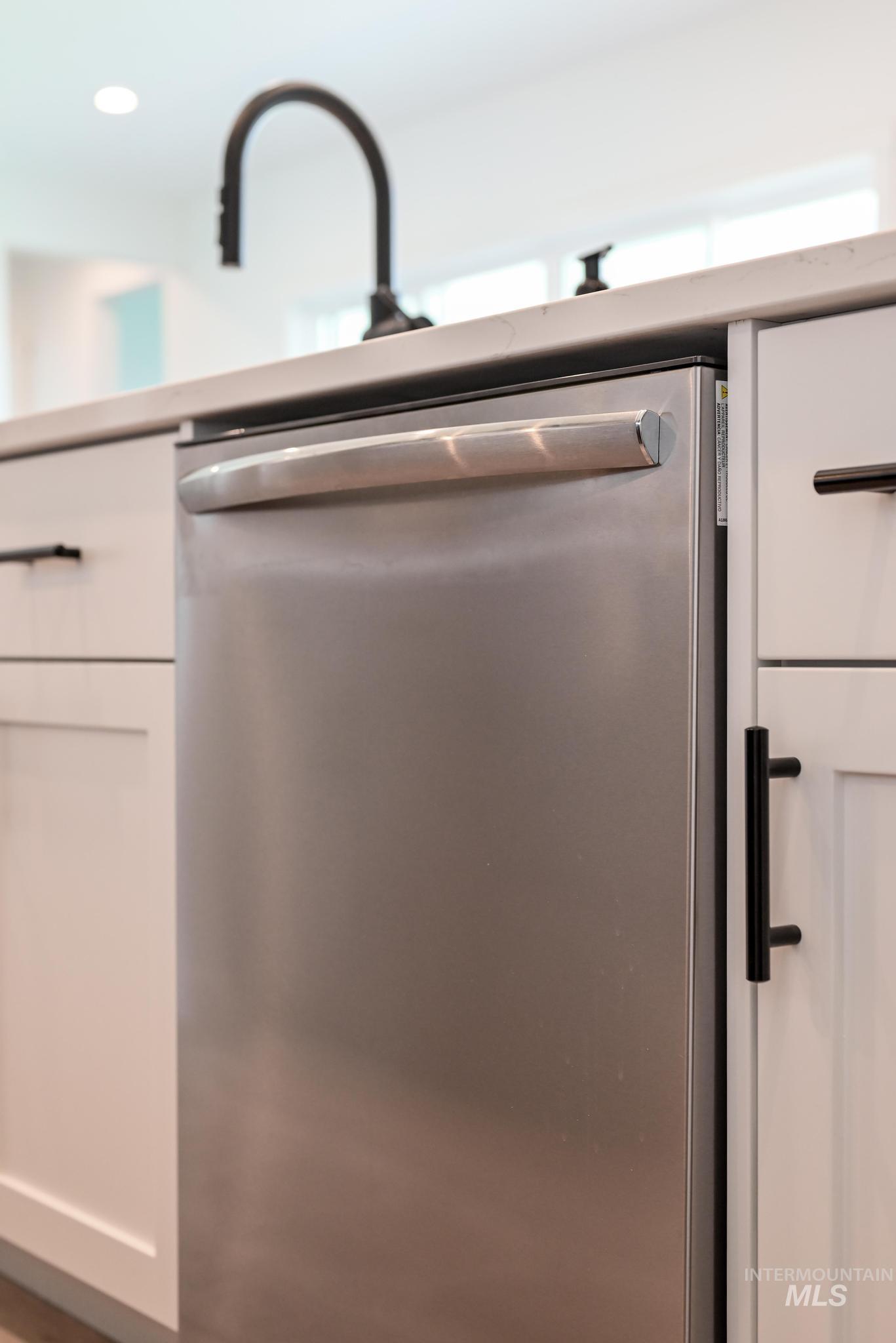 Kitchen view of stainless steel dishwasher, white cabinets, and recessed lighting