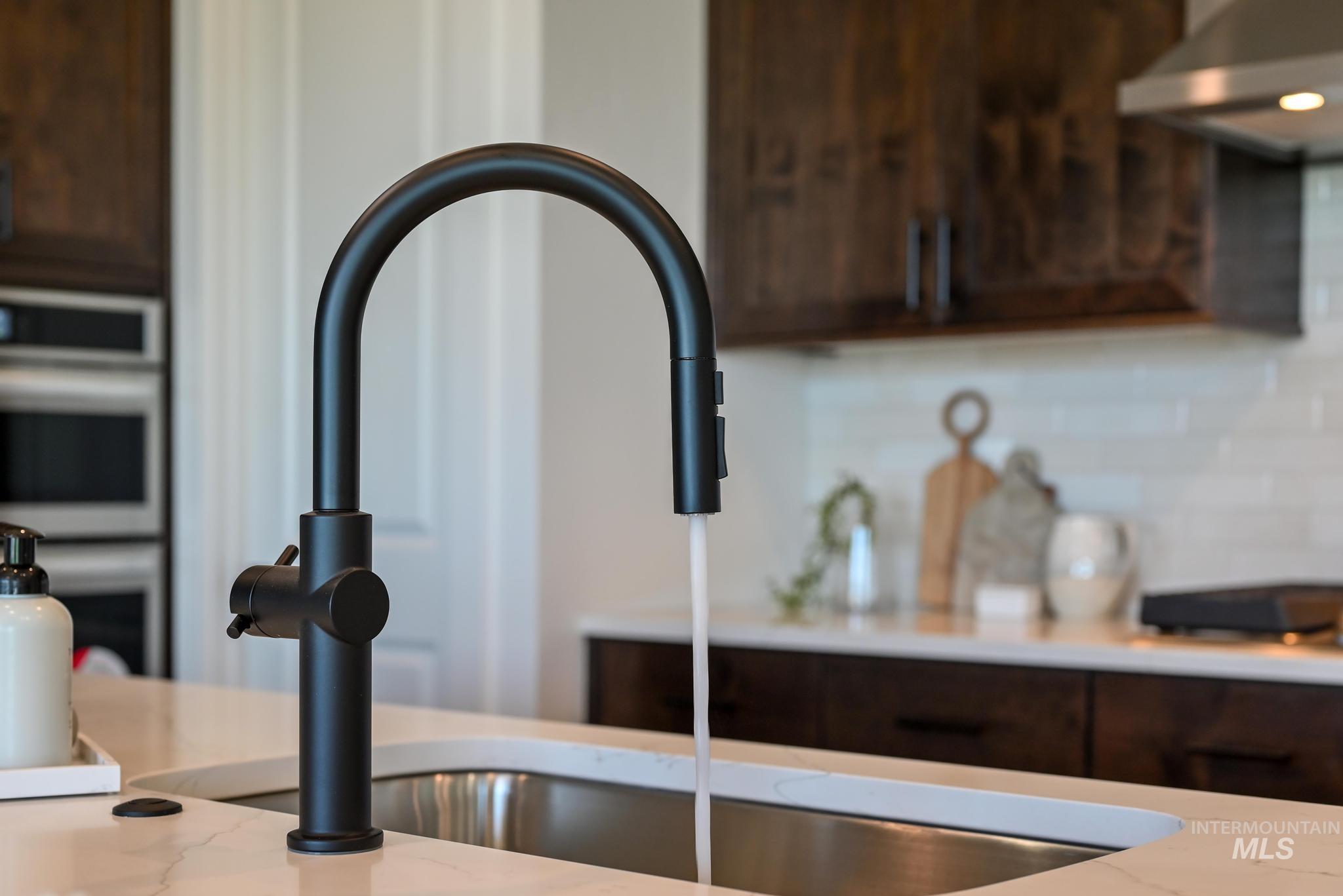 Kitchen view of under cabinet range hood, dark brown cabinetry, double oven, and decorative backsplash