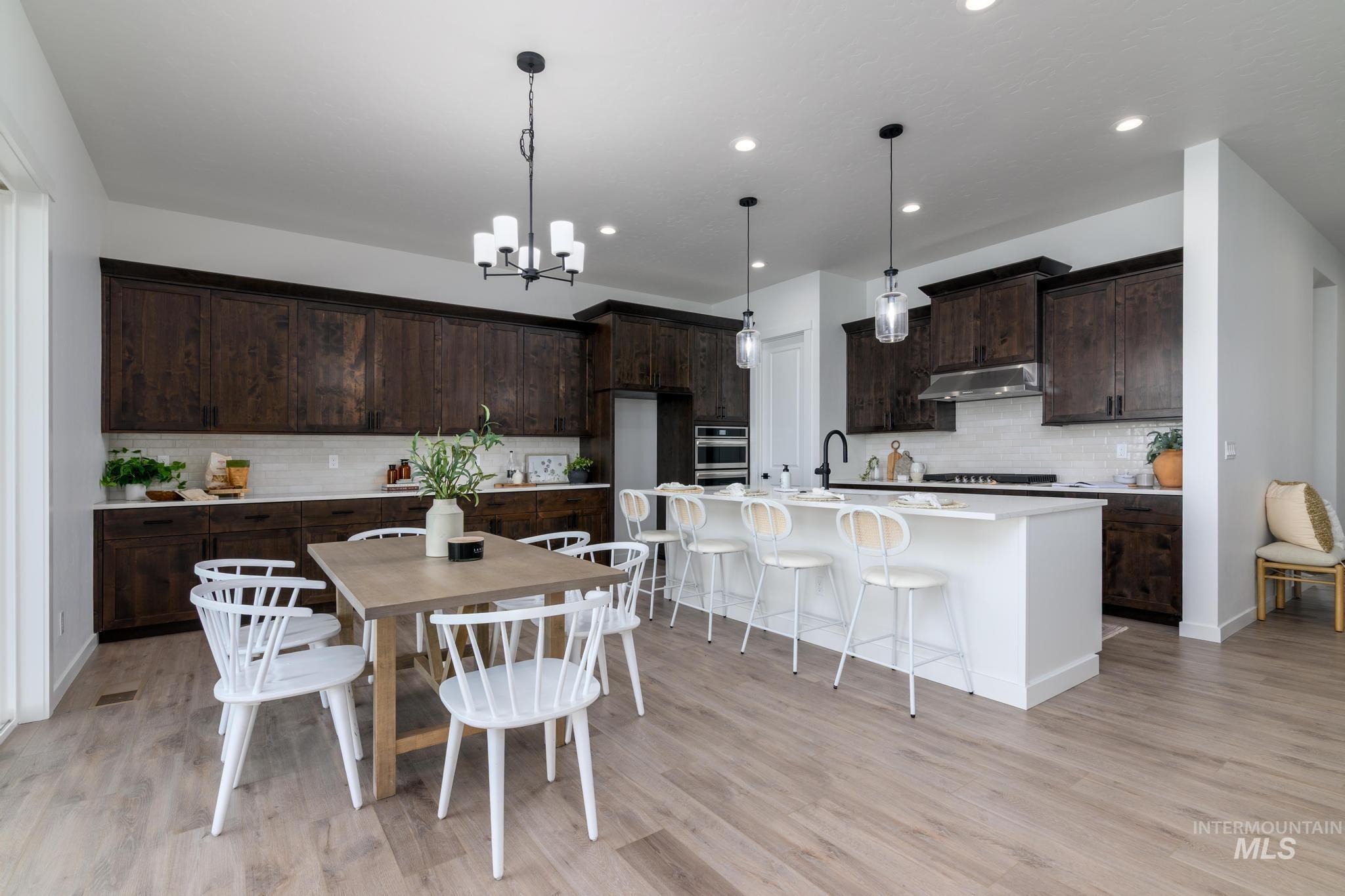 Kitchen with ventilation hood, decorative backsplash, dark brown cabinets, a chandelier, and light wood-type flooring