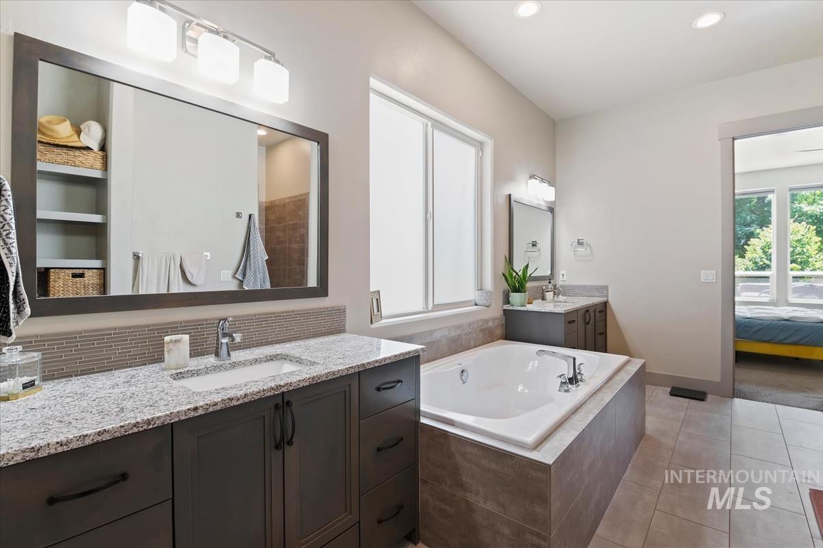 Bathroom featuring a built-in soaking tub, dual vanity with granite countertops, integrated sinks, and tiled flooring