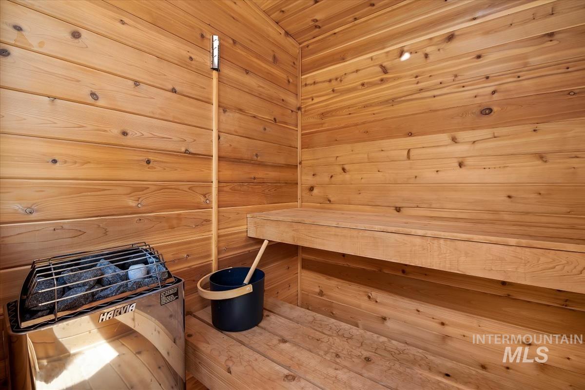 Wood-paneled sauna featuring a built-in heater with visible stones, integrated wood benches, and a wall-mounted light fixture