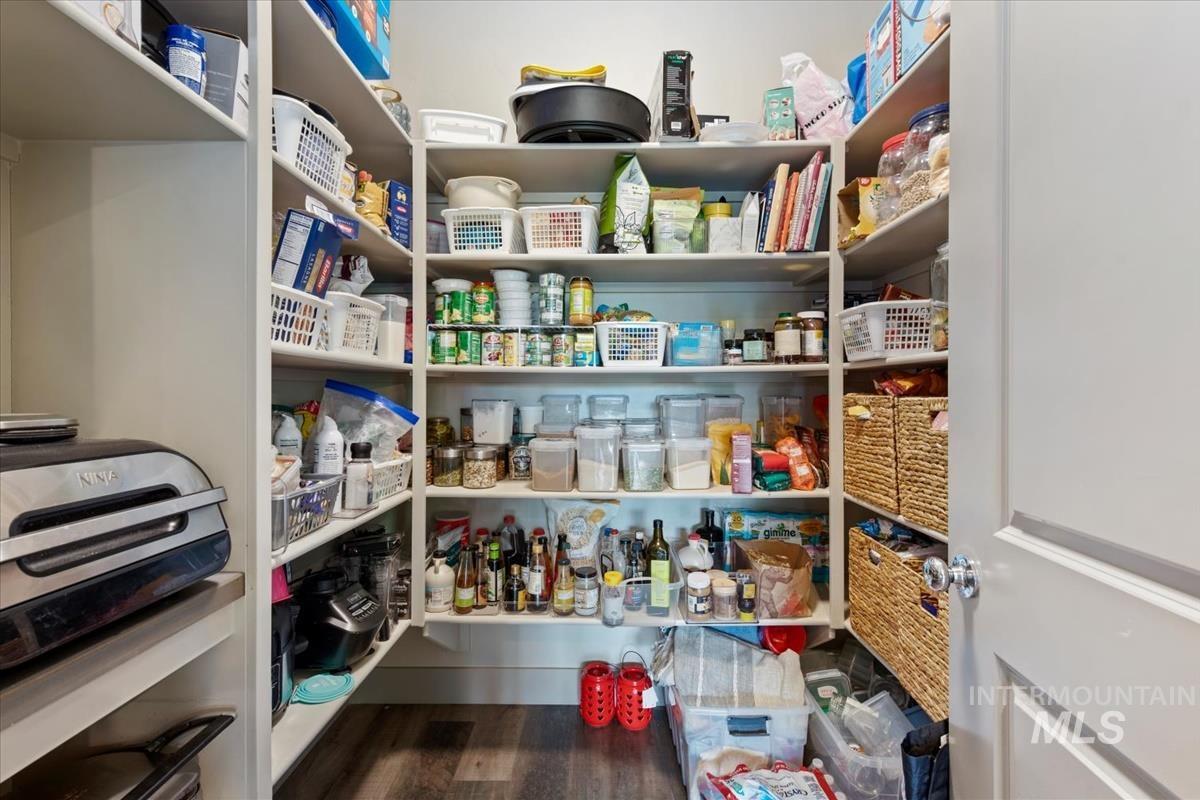 Walk-in pantry featuring extensive built-in shelving, durable wood-finish flooring, and a paneled door with a glass knob