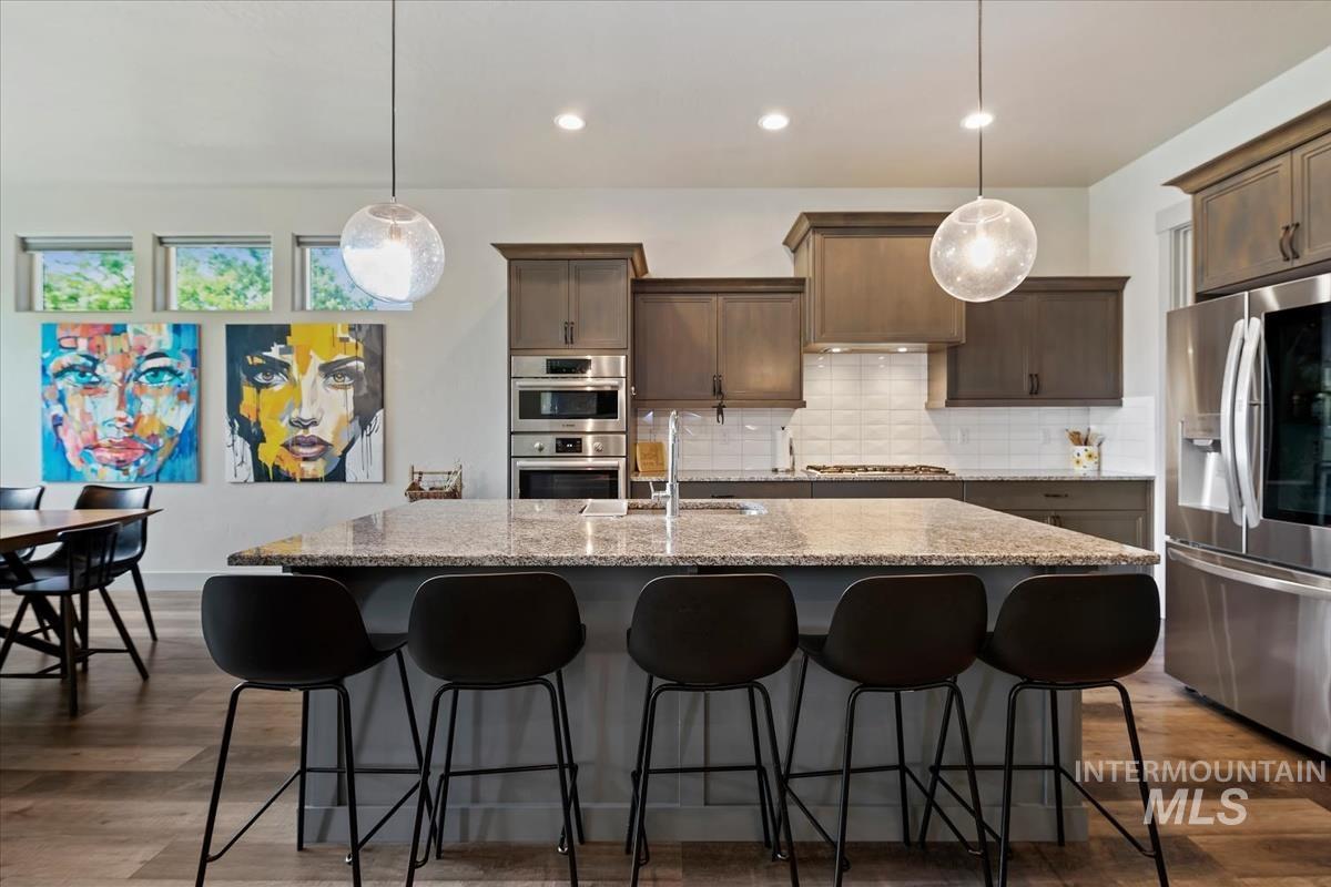 Kitchen featuring an oversized island with countertop seating, stone countertops, wood-finish flooring, stainless steel appliances, and suspended pendant lighting