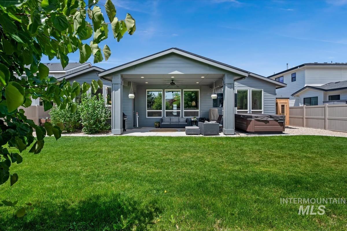 Expansive backyard featuring a manicured lawn, covered patio, outdoor ceiling fan, and a hardscaped area with a built-in hot tub