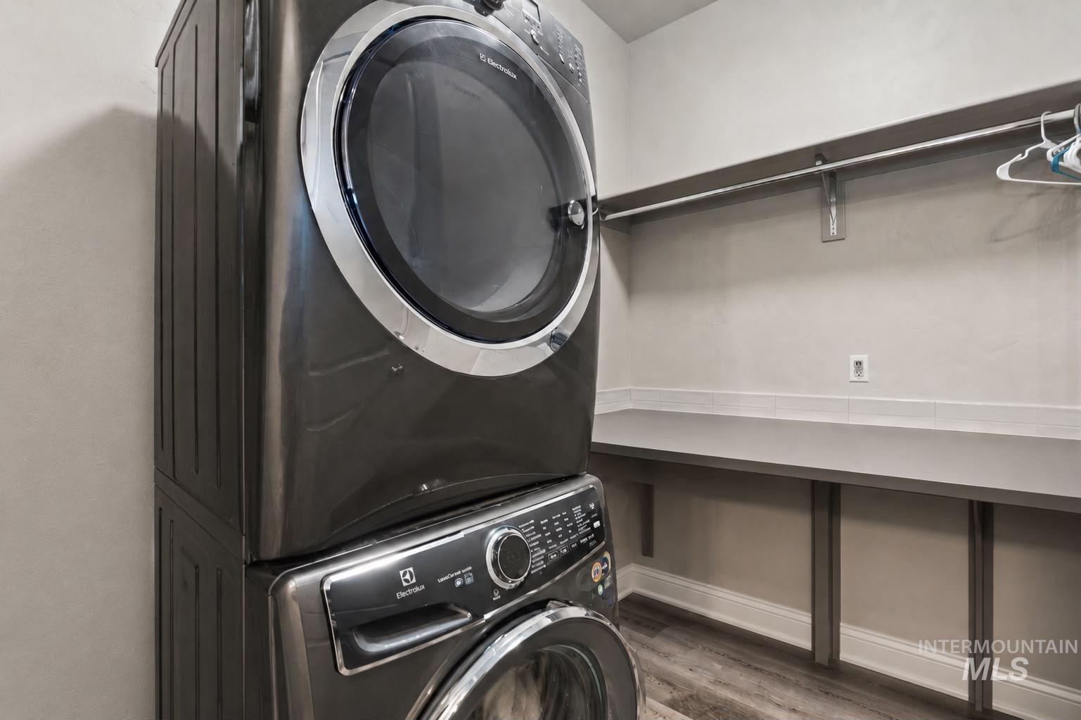 Laundry area featuring a stacked washer and dryer, wood-finish flooring, a built-in folding counter, and a garment rod
